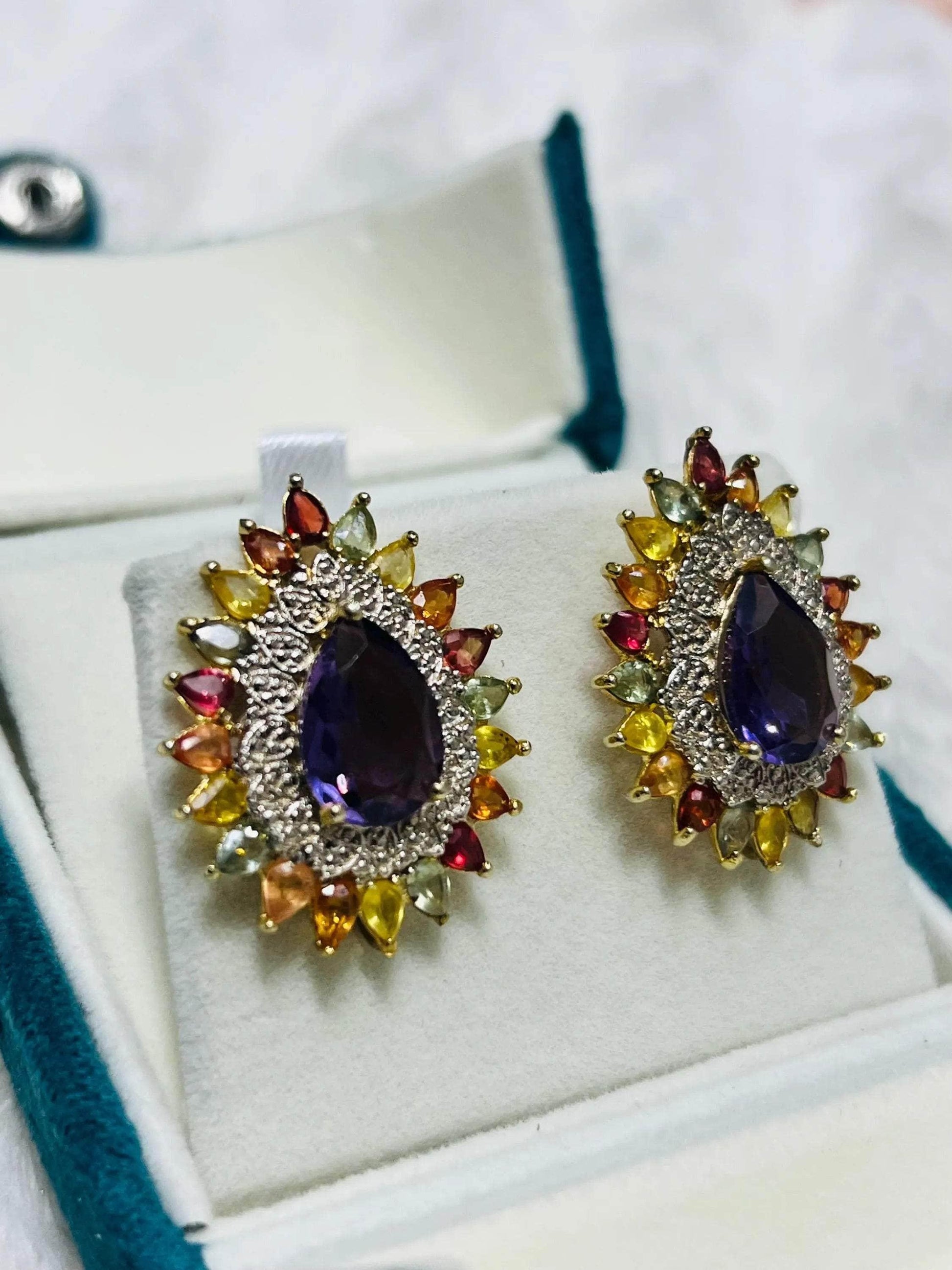  Close-up of two stunning handmade amethyst and colorful sapphire sunburst earrings in a teal velvet box.