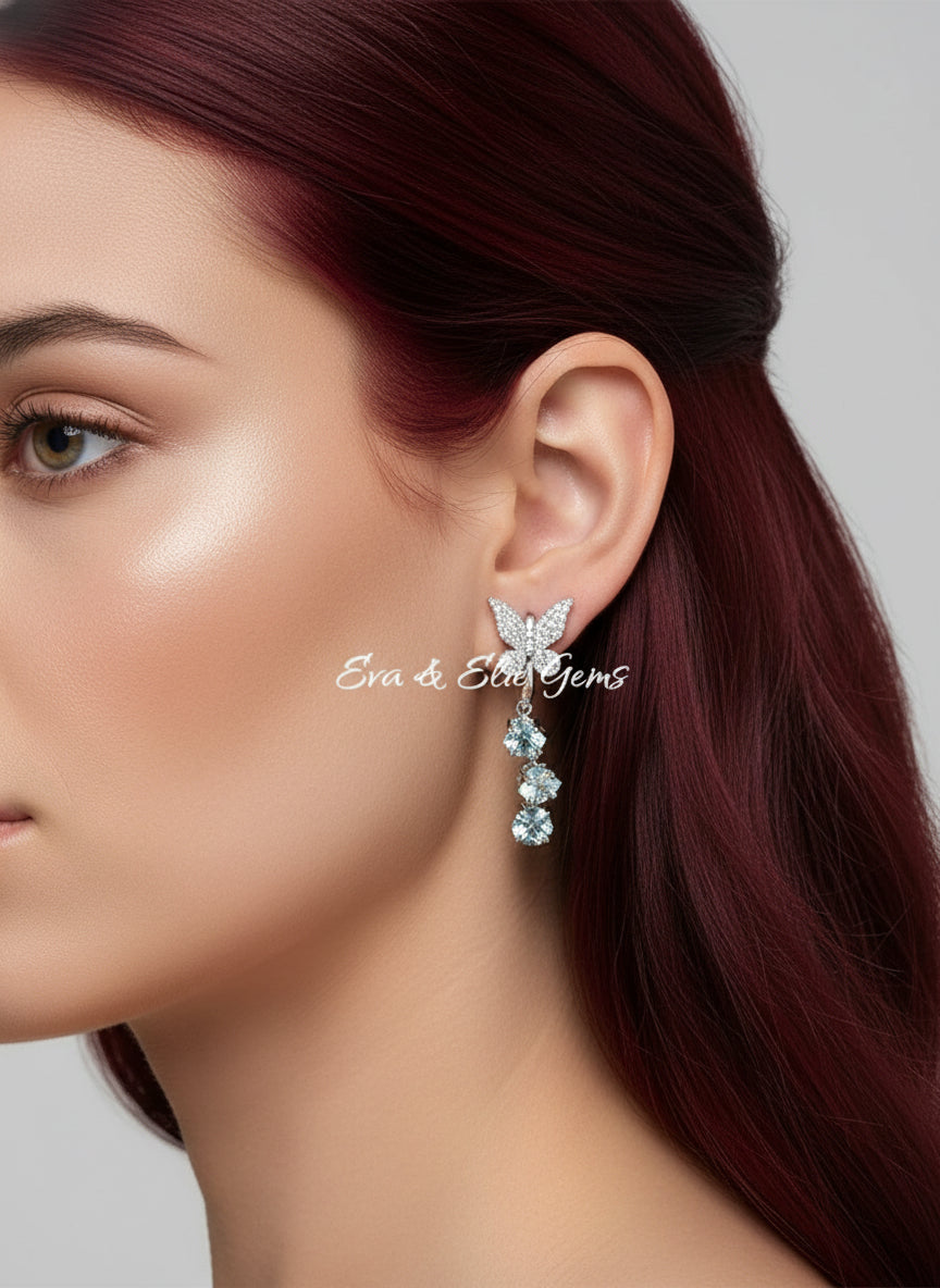 A model wearing beautiful new butterfly earrings with sparkling cubic zirconia and three light blue gemstones.