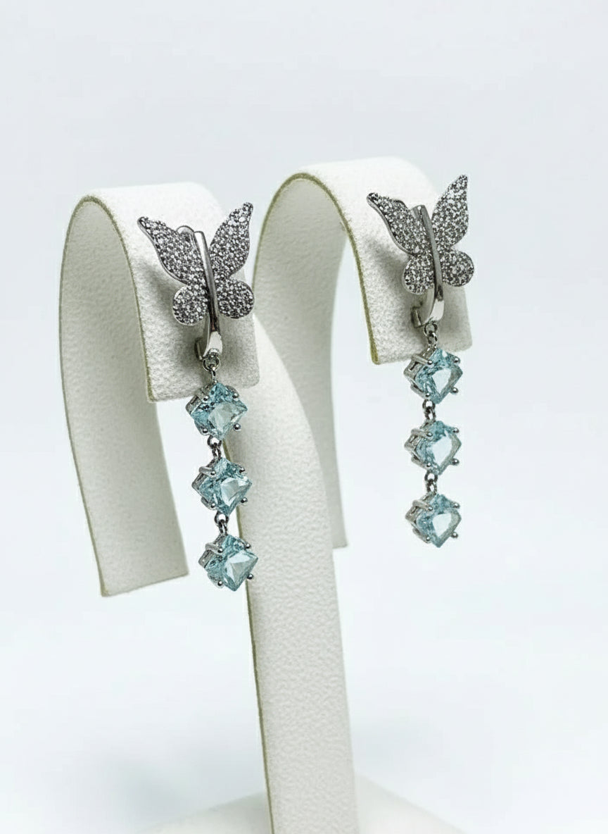  A pair of beautiful new butterfly dangle earrings with light blue square gemstones, presented on a white display.