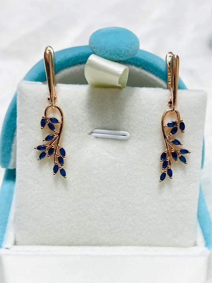 Elegant dangle earrings featuring a leaf design with marquise-cut blue sapphires, set in 14K rose gold.
