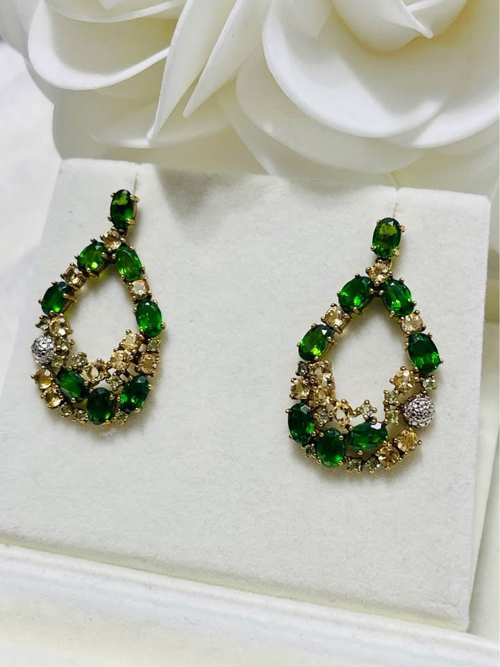 Closeup of handmade chrome diopside and yellow sapphire teardrop earrings on a white display.