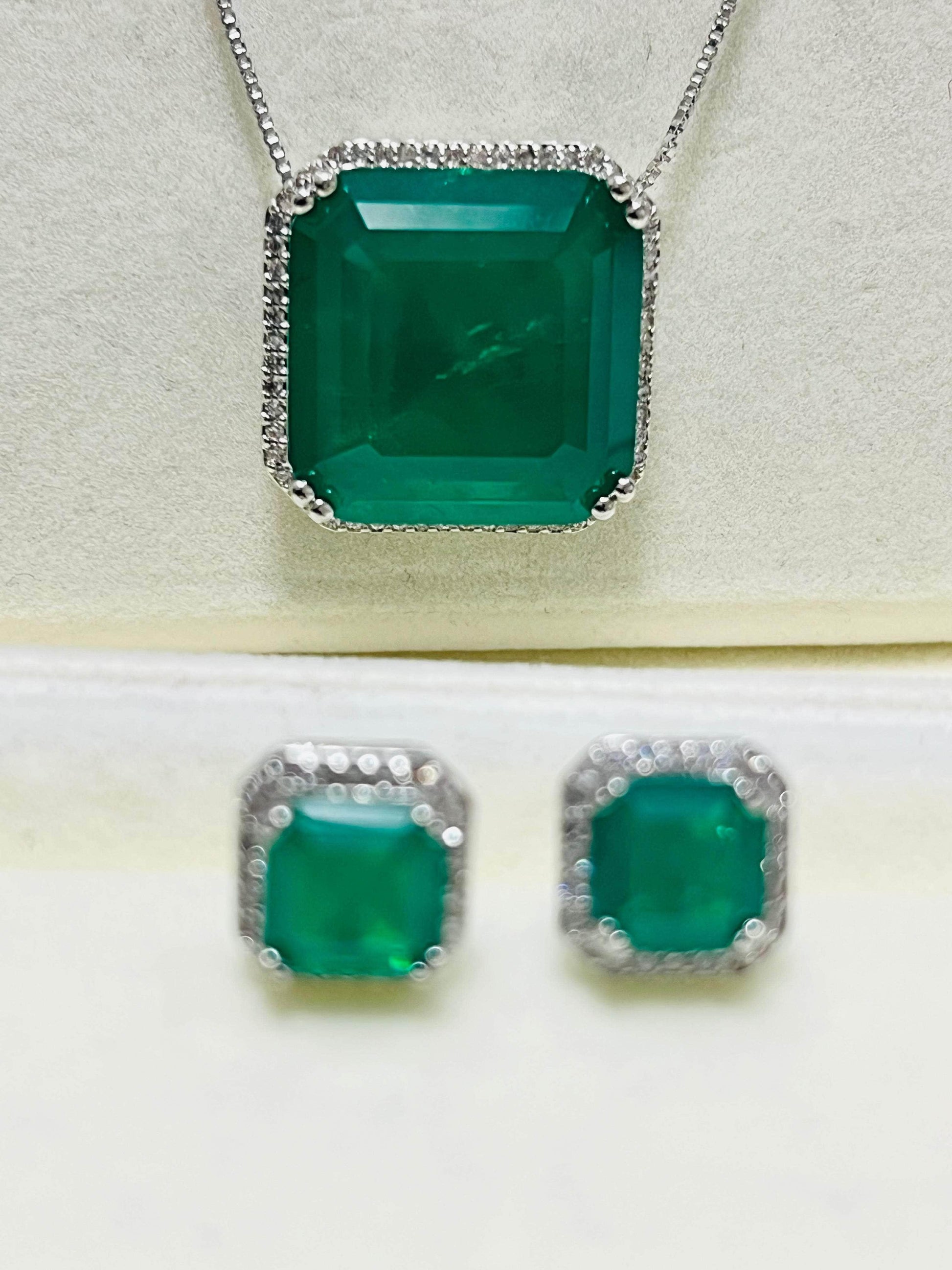 Detailed view of a striking emerald pendant necklace and matching earrings with diamond halos, slightly blurred focus.