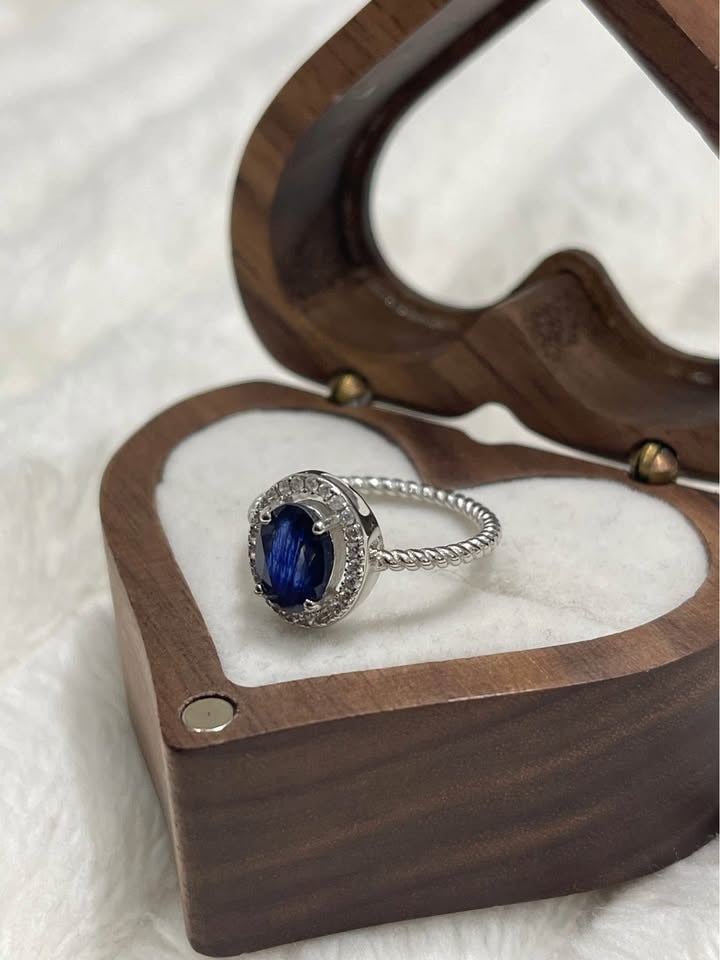 Close-up of a natural blue sapphire solitaire ring with a diamond halo on a twisted silver band.