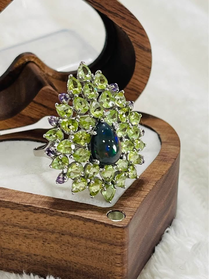 A close-up of a pear-shaped black fire opal ring surrounded by sparkling peridot and amethyst gems.