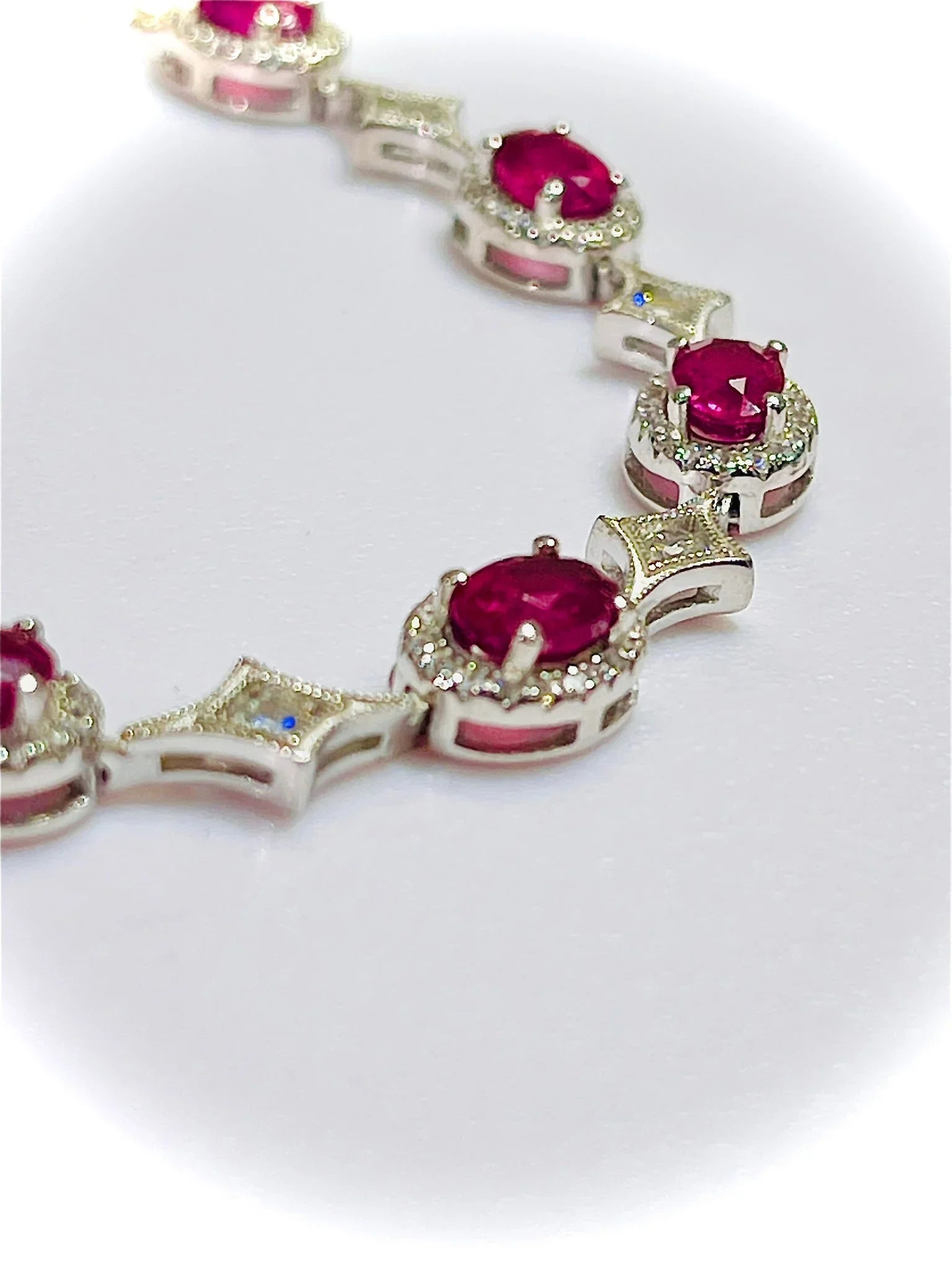 Detailed close-up of a silver bracelet, showing brilliant oval rubies, sparkling diamond accents, and intricate metalwork.