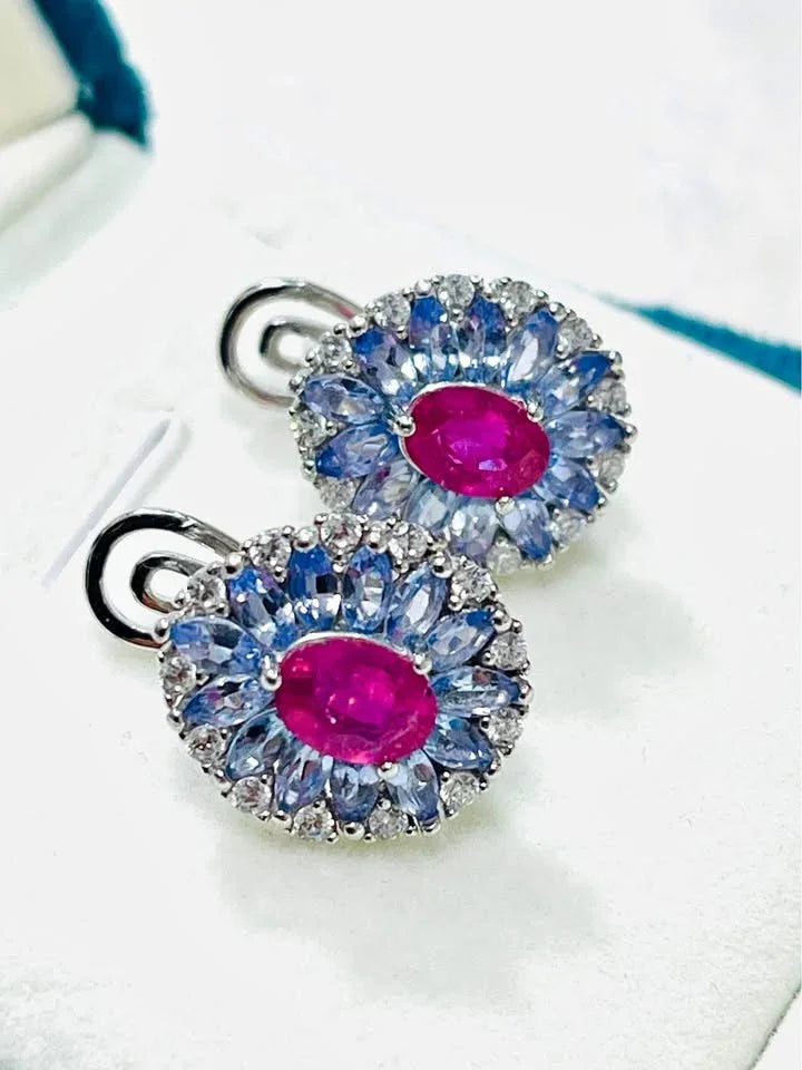 A close-up of a pair of stunning sterling silver earrings featuring natural tanzanite and central ruby stones.