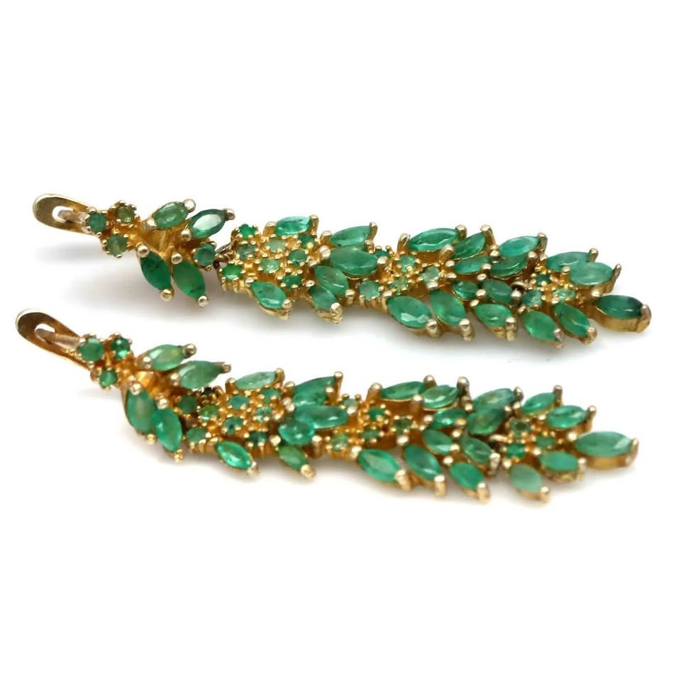 Long, leafy dangle earrings featuring natural Colombian emeralds set in gold, on a white background.