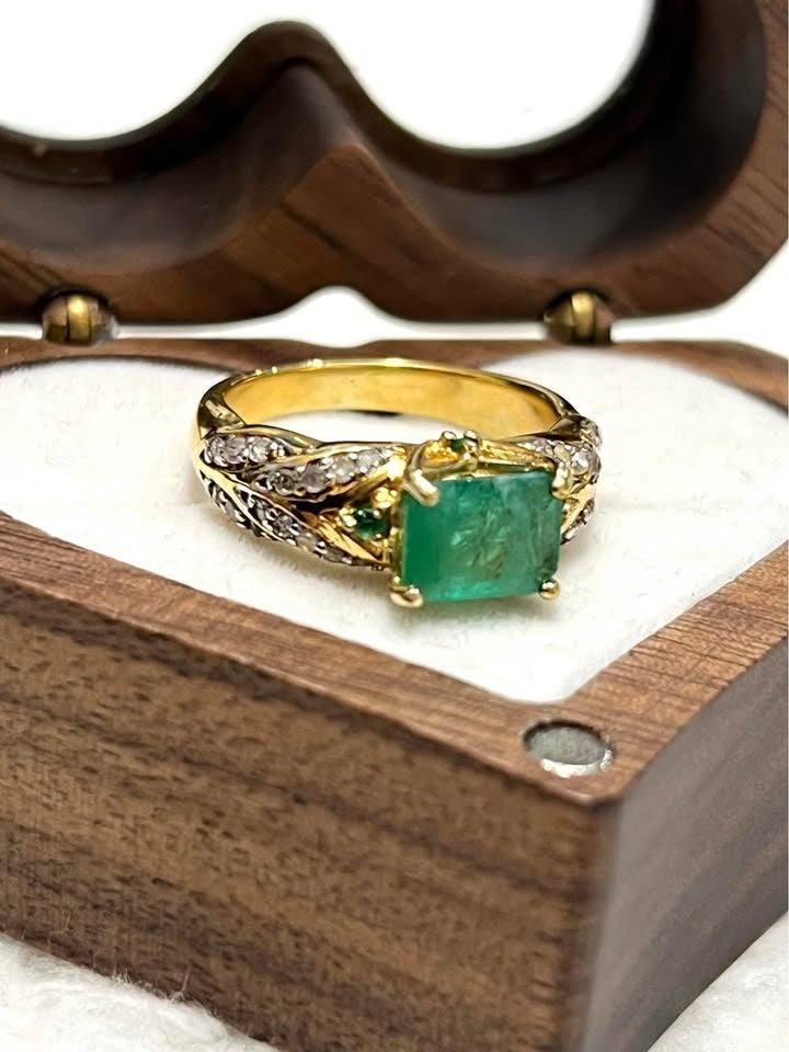 Close-up of a natural Colombian emerald ring with diamond accents and gold setting, side view.