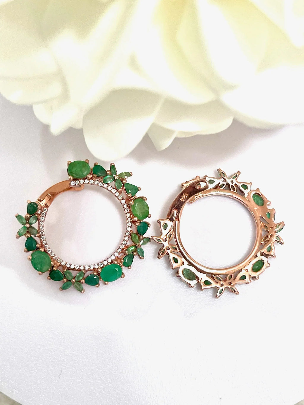 Two rose gold plated sterling silver hoop earrings with clear Colombian emeralds in various cuts, viewed from the top