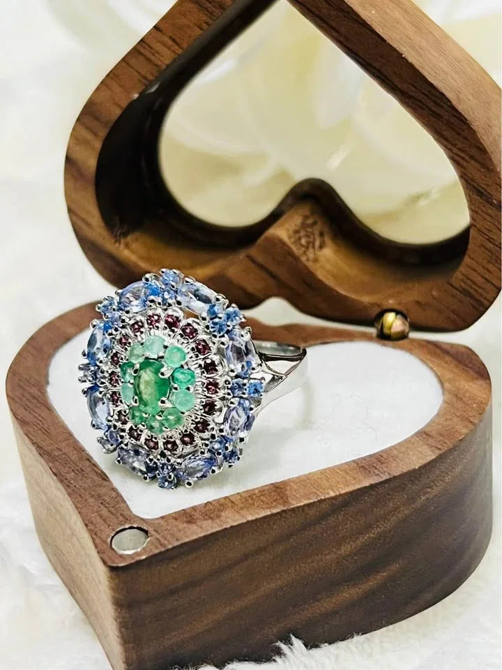 An elegant ring with emerald, rhodolite, and tanzanite gemstones, presented in a decorative jewelry box.