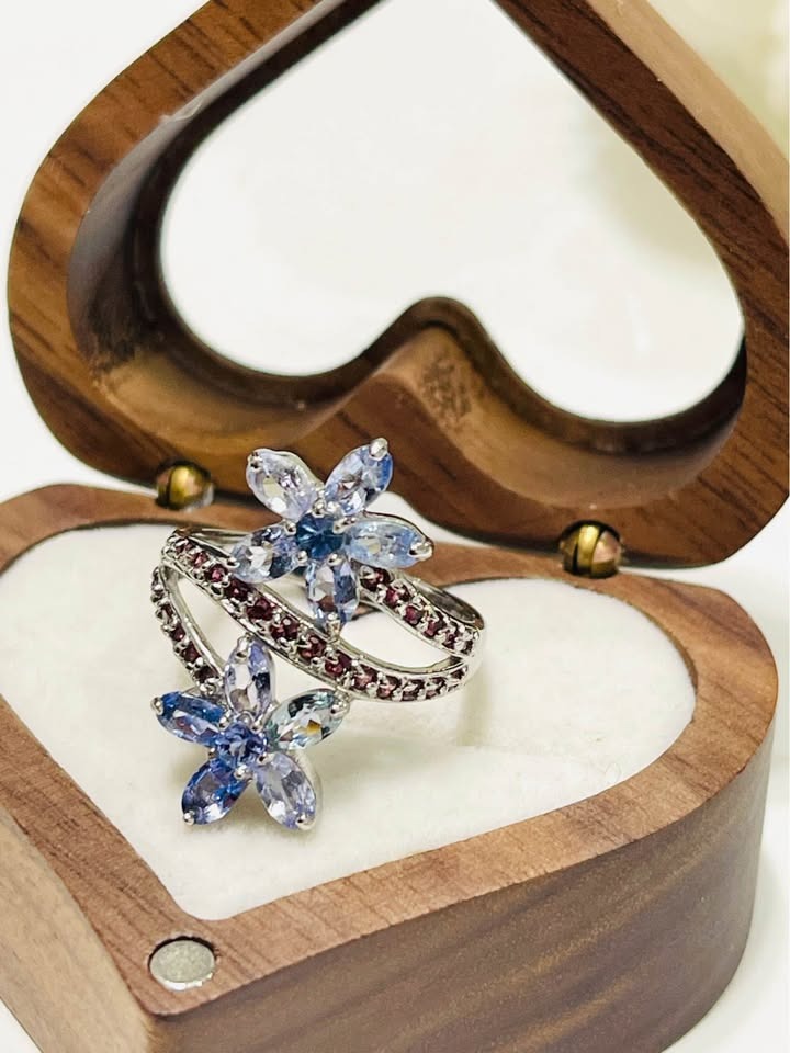 An elegant natural tanzanite and rhodolite ring, showcasing its floral design in a wooden jewelry box.