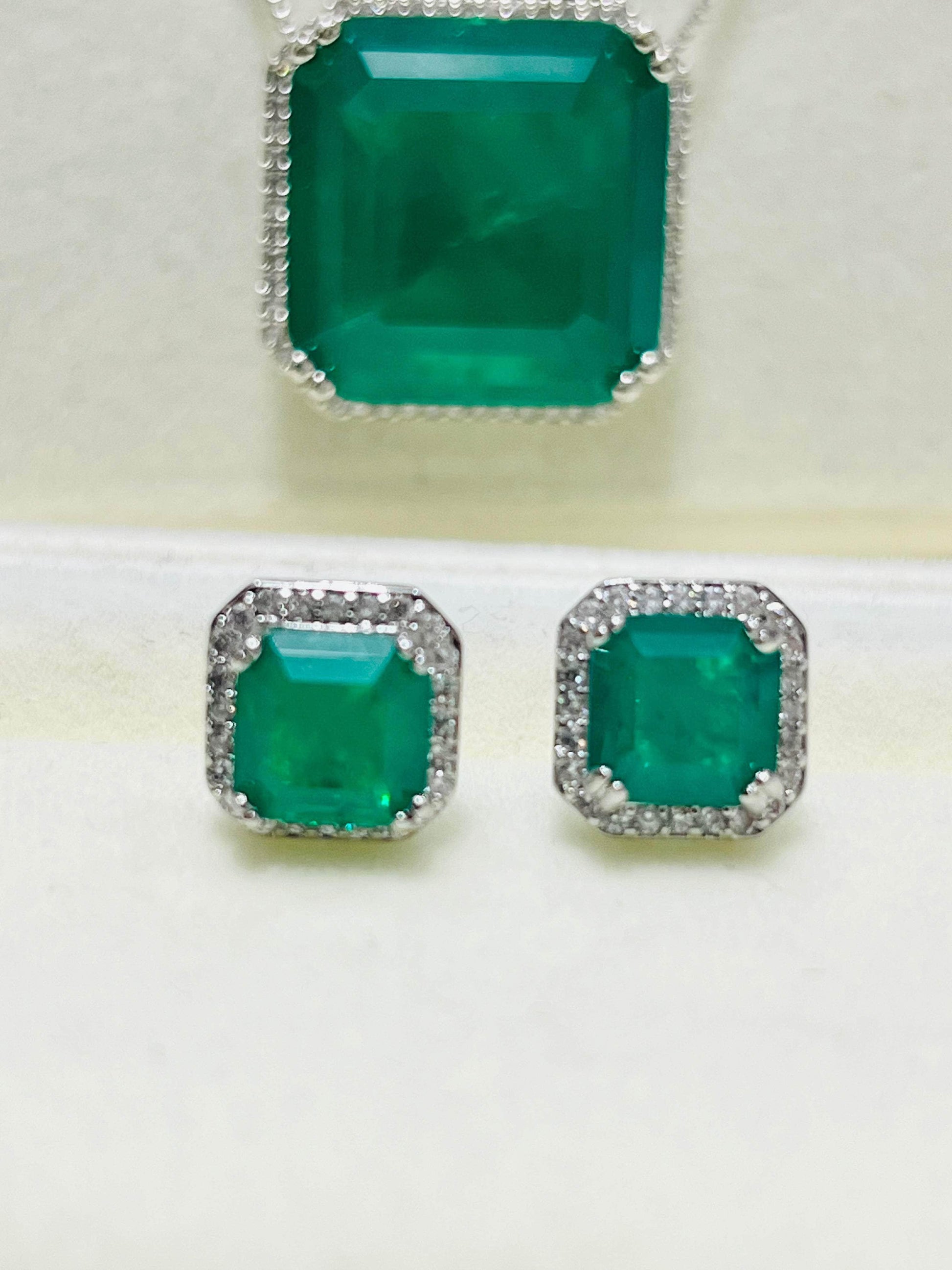 Close-up of a stunning emerald cut necklace and matching earrings, each framed with a sparkling diamond halo