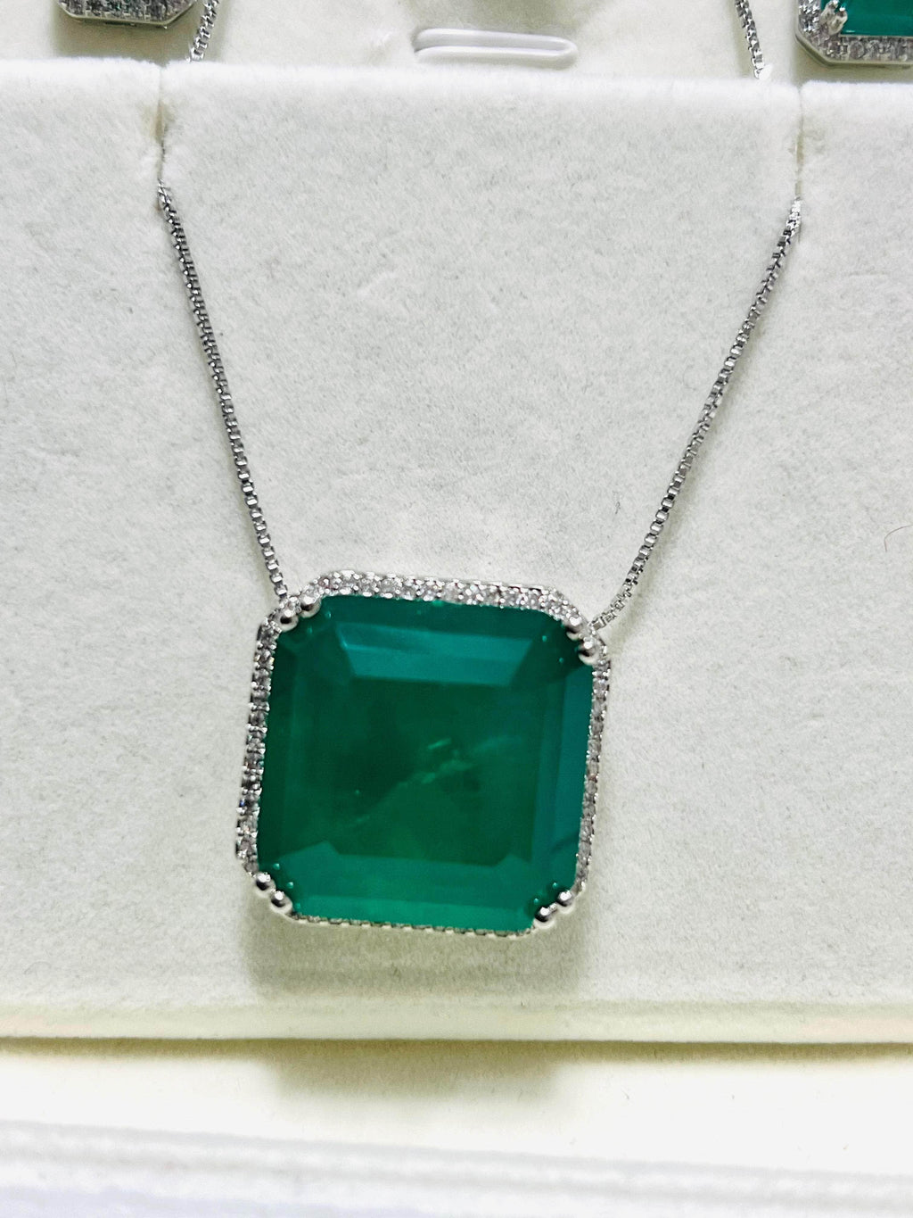 Close-up of a beautiful emerald cut necklace, featuring a vibrant green stone surrounded by a sparkling diamond halo.