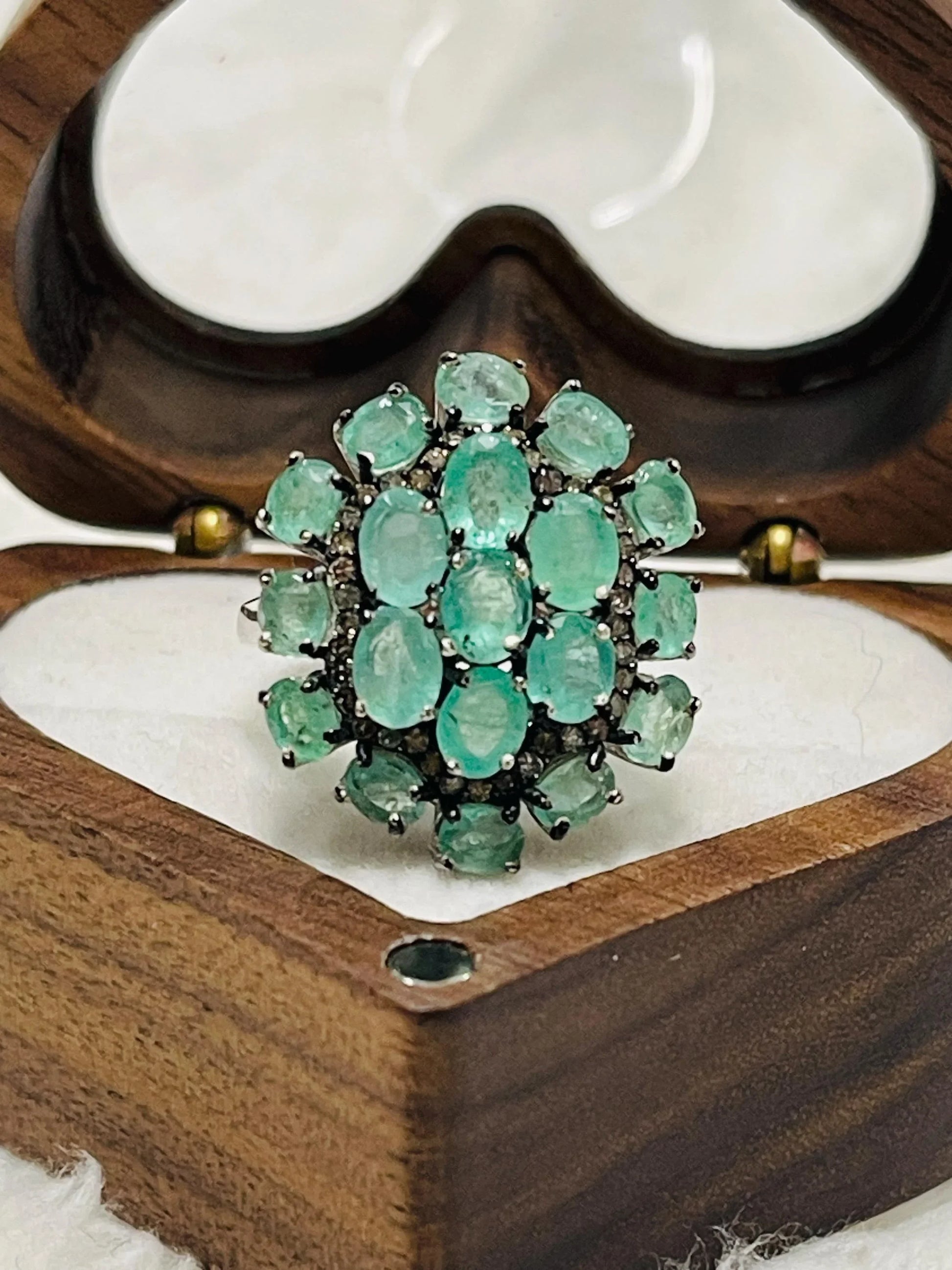 Luxurious emerald and diamond cluster ring worn on a finger, displaying its sparkle and elegant design.