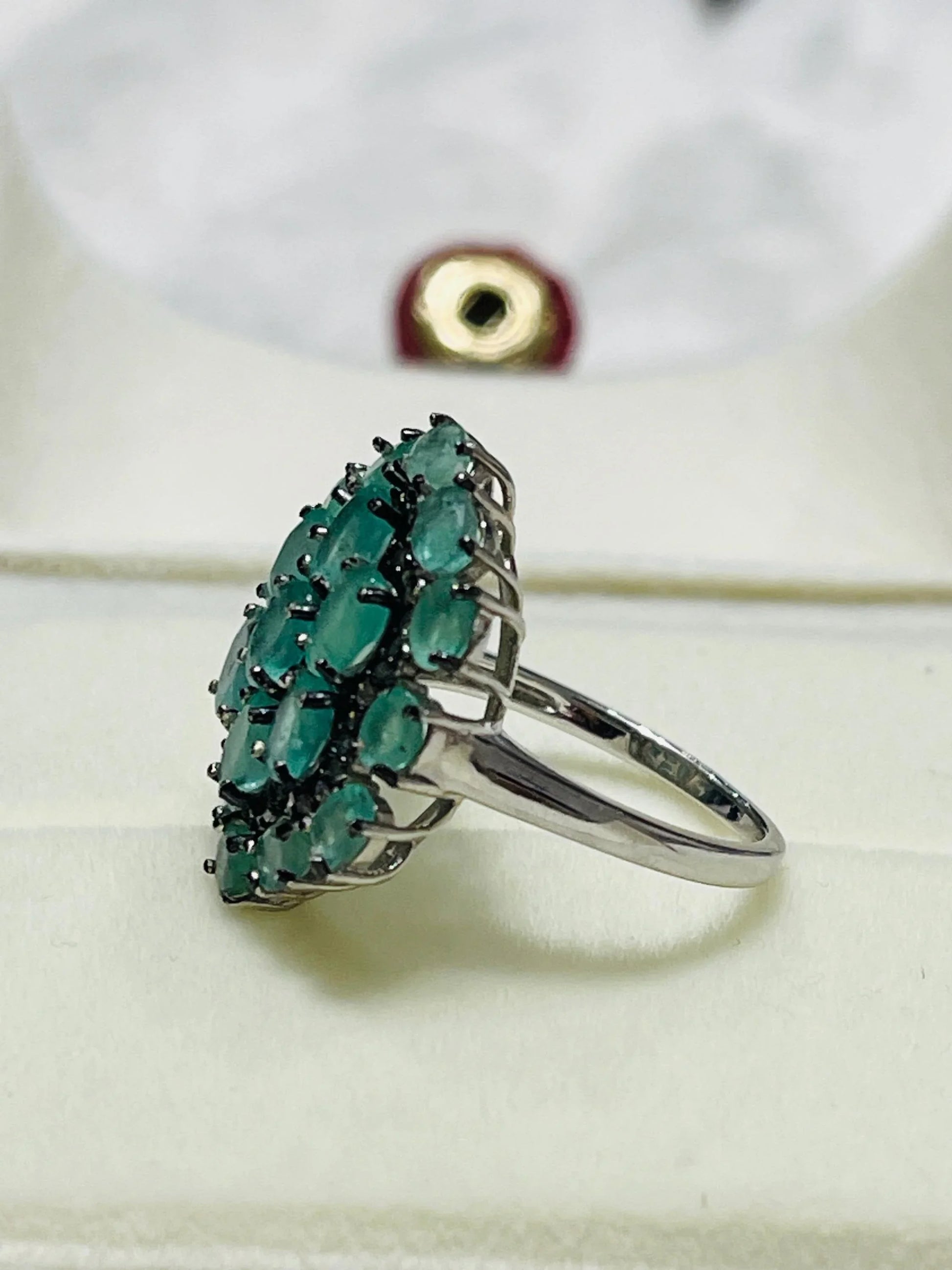 Side profile of an elegant emerald and diamond cluster ring, highlighting its sterling silver band and raised setting.