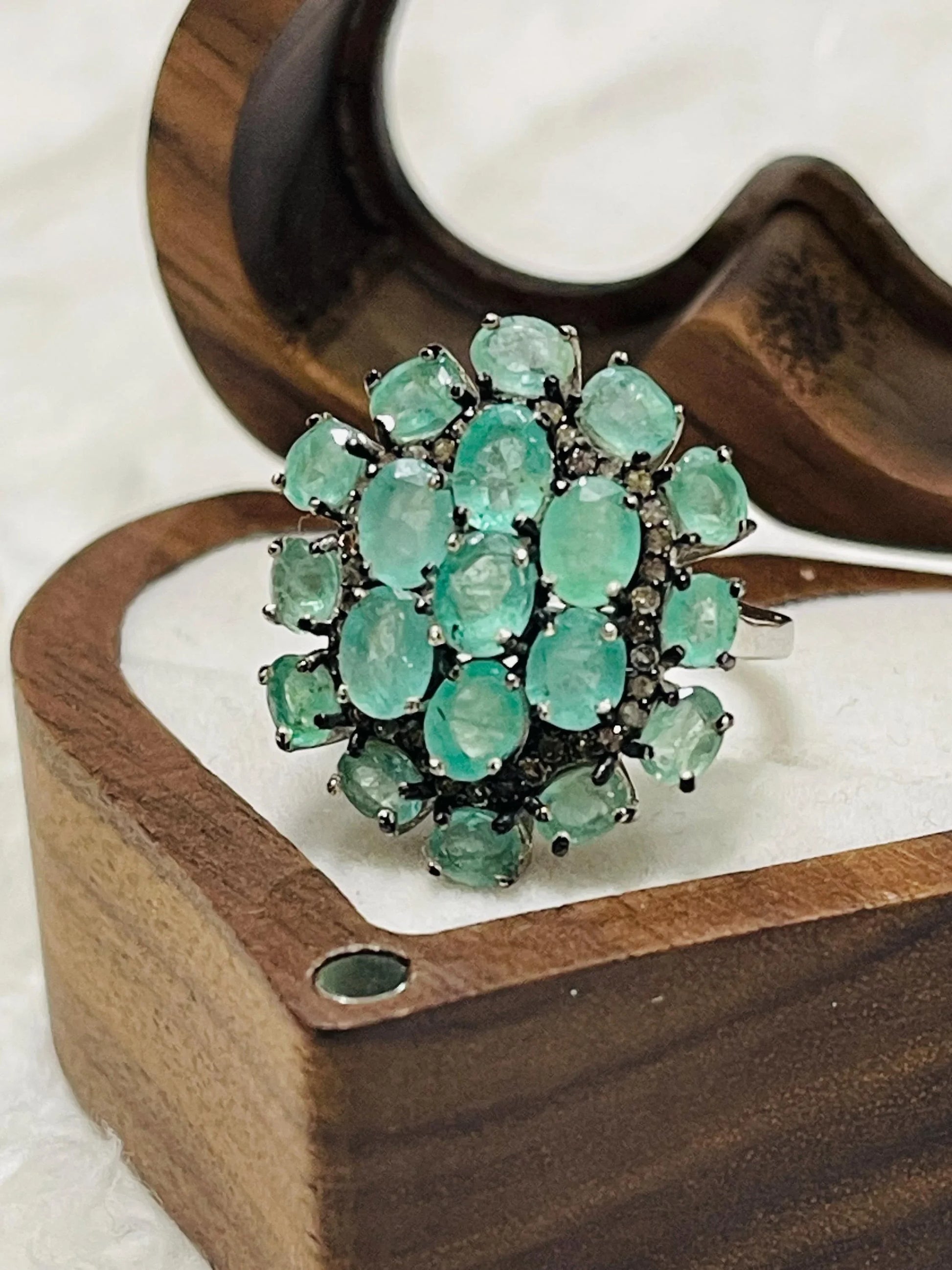 Emerald and diamond cluster ring next to a ring sizer, indicating its size for accurate fitting.