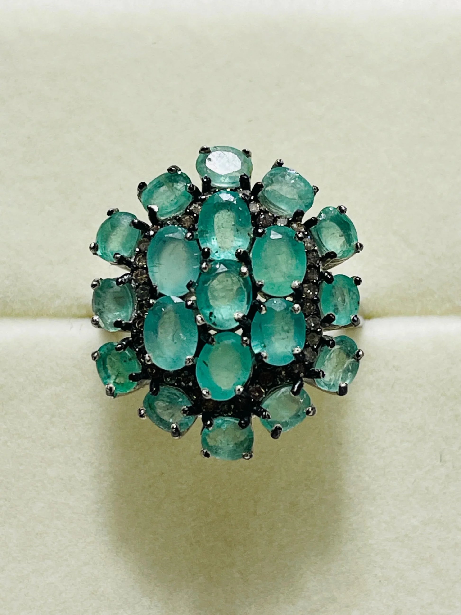 Exquisite oval emerald and diamond cluster ring in sterling silver, displayed on a black velvet stand.