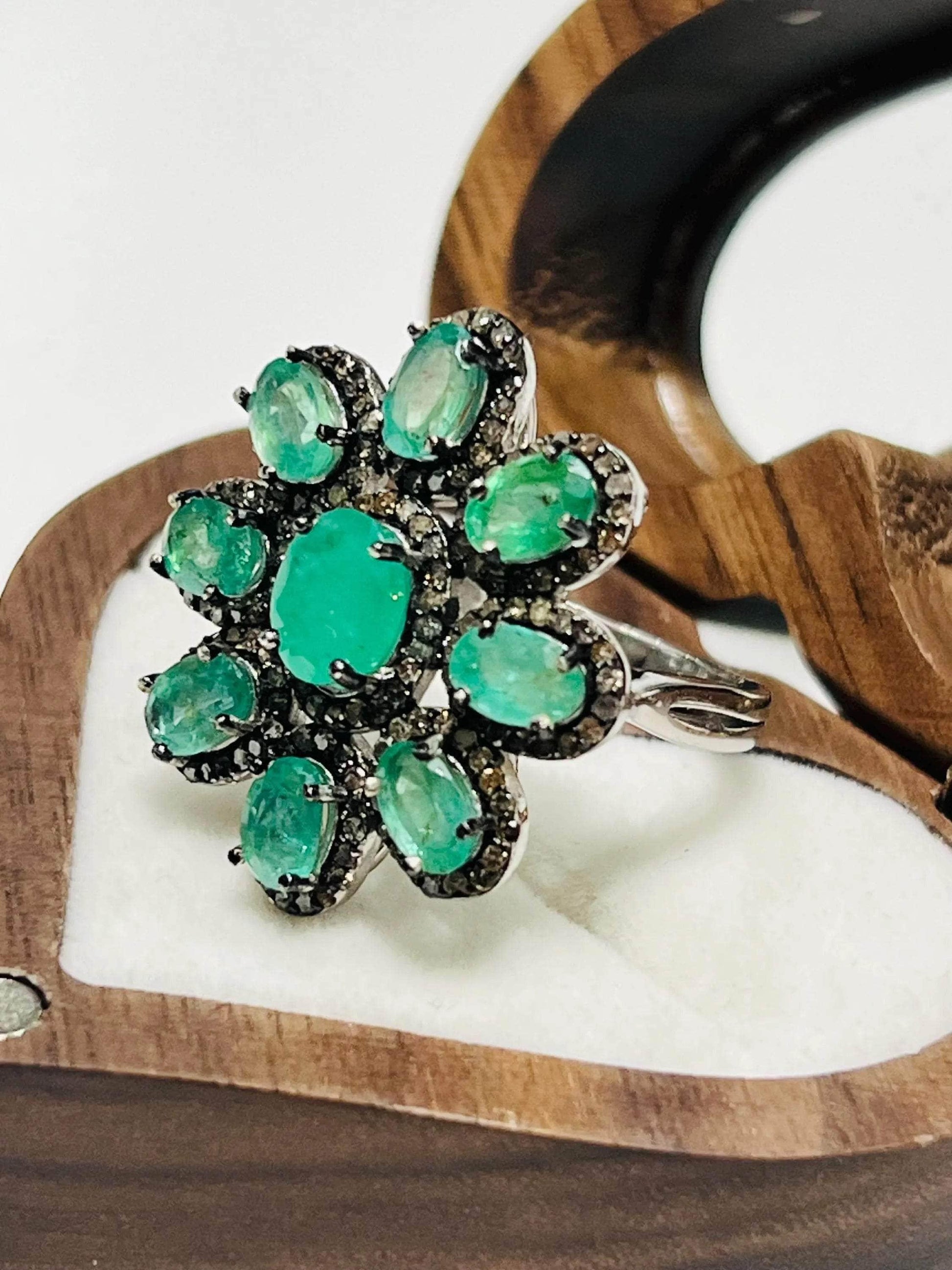 Angled view of a beautiful emerald and diamond floral cluster ring, showcasing its intricate design.