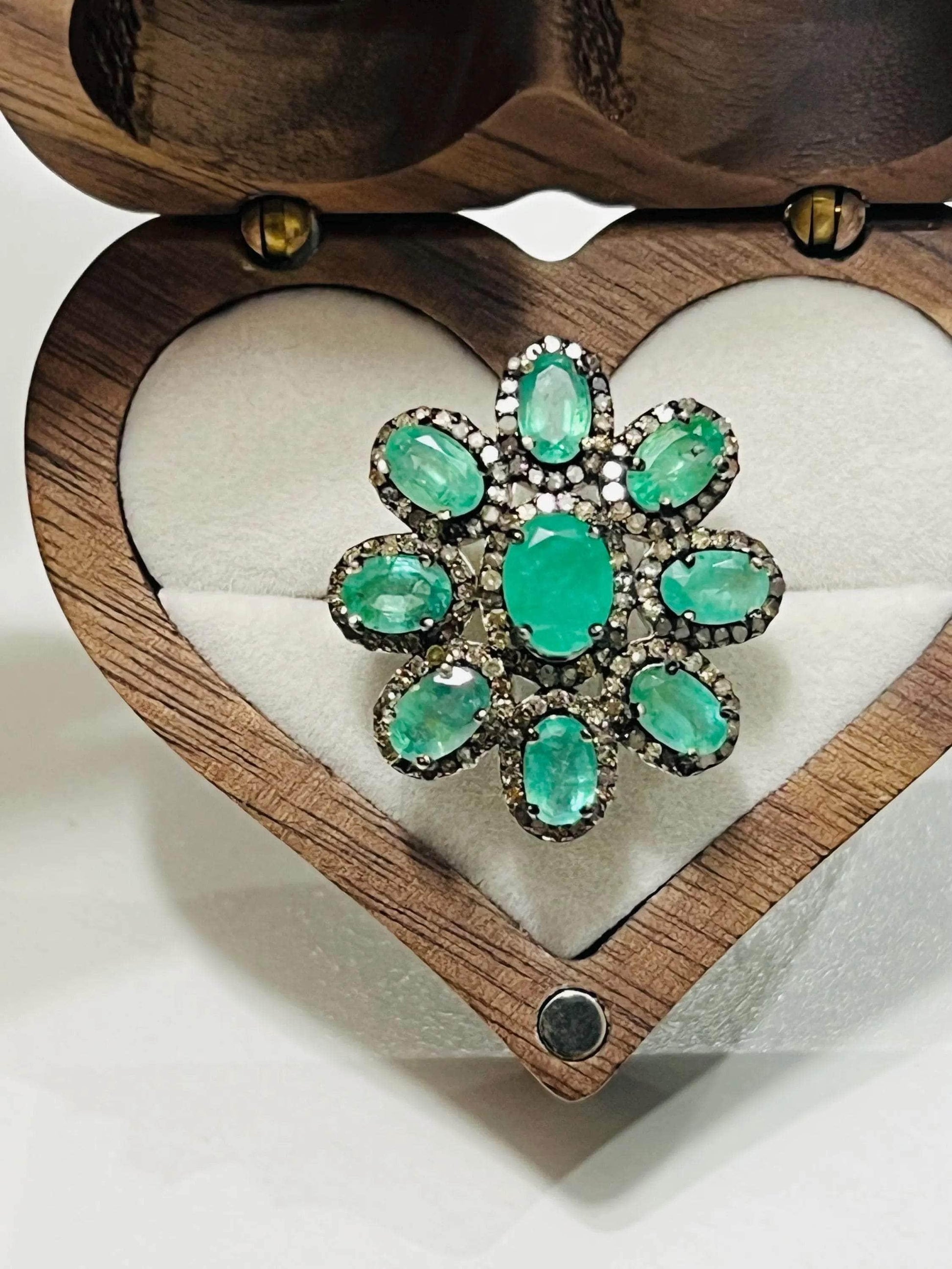 Side profile of an elegant emerald and diamond floral ring, highlighting the detailed setting and band.