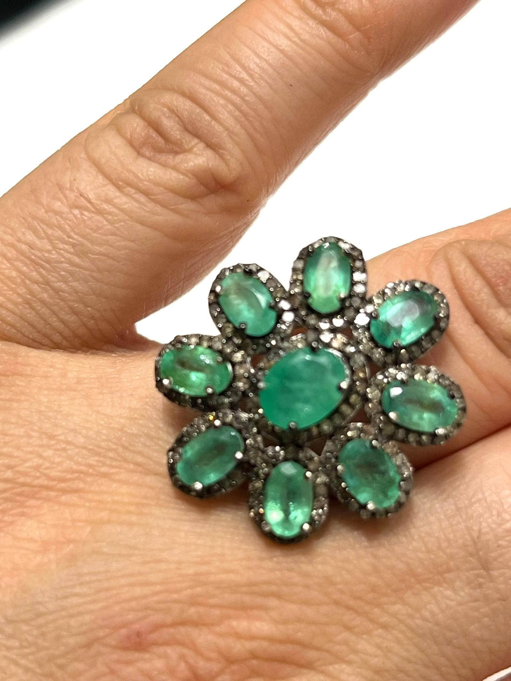 Top-down view of a stunning emerald and diamond floral ring, emphasizing the vibrant green and brilliant sparkle.