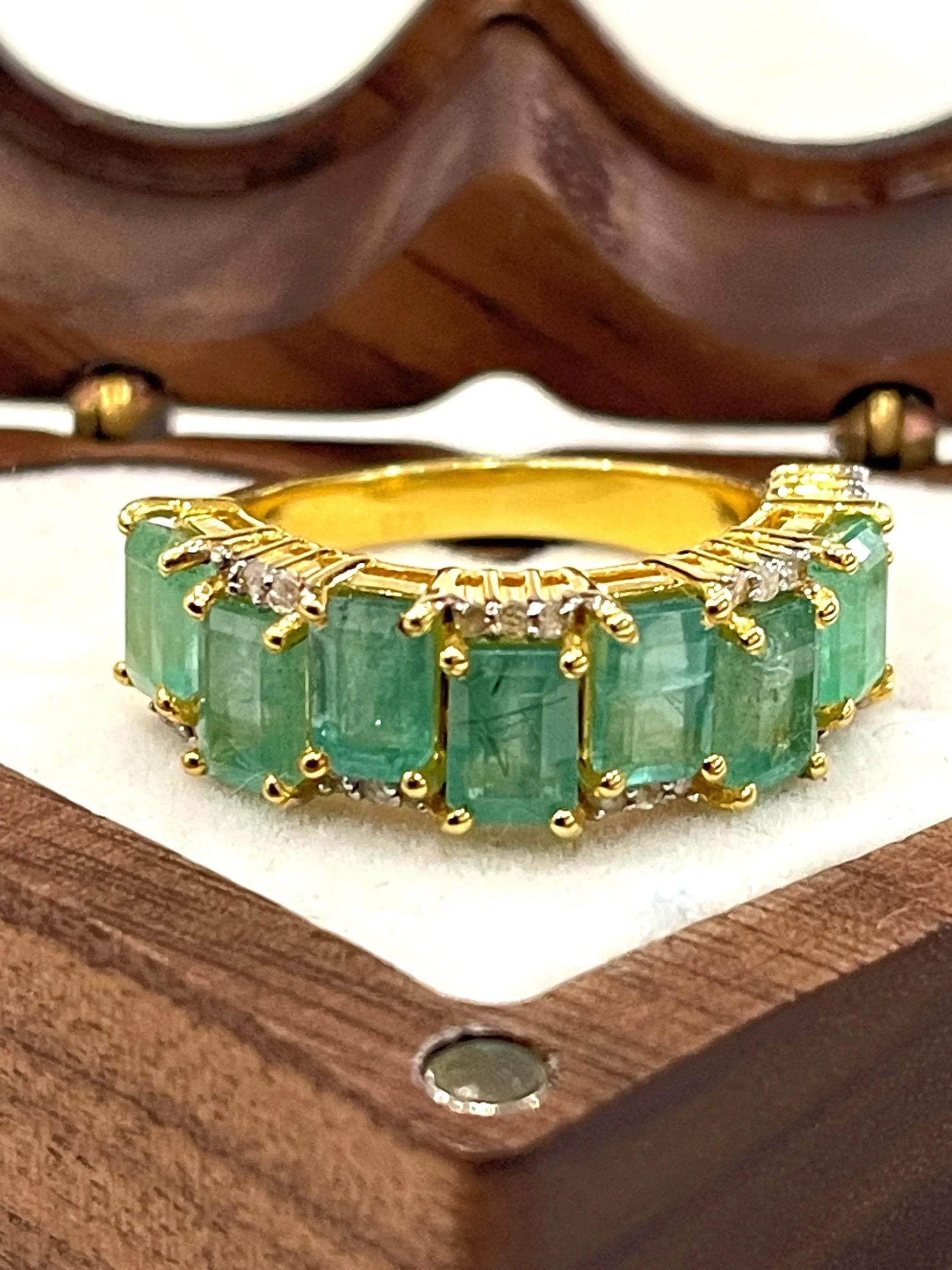 Exquisite floral ring with a central emerald gemstone surrounded by sparkling diamonds, displayed on a white stand.