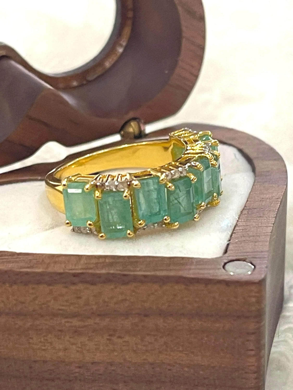  Side profile of an elegant emerald and diamond flower ring, highlighting the detailed silver setting and band.