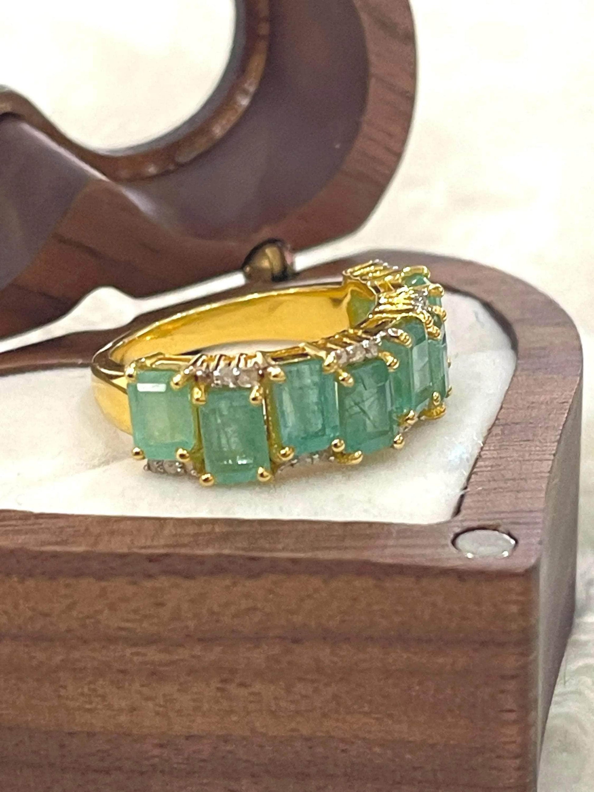  Side profile of an elegant emerald and diamond flower ring, highlighting the detailed silver setting and band.