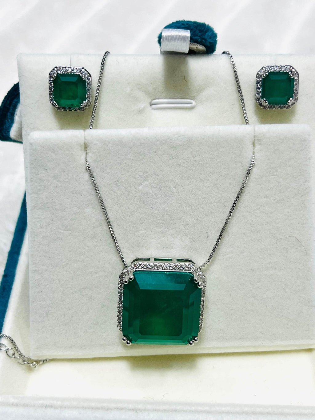 Emerald and diamond jewelry set including a necklace and earrings, neatly displayed in a white gift box.