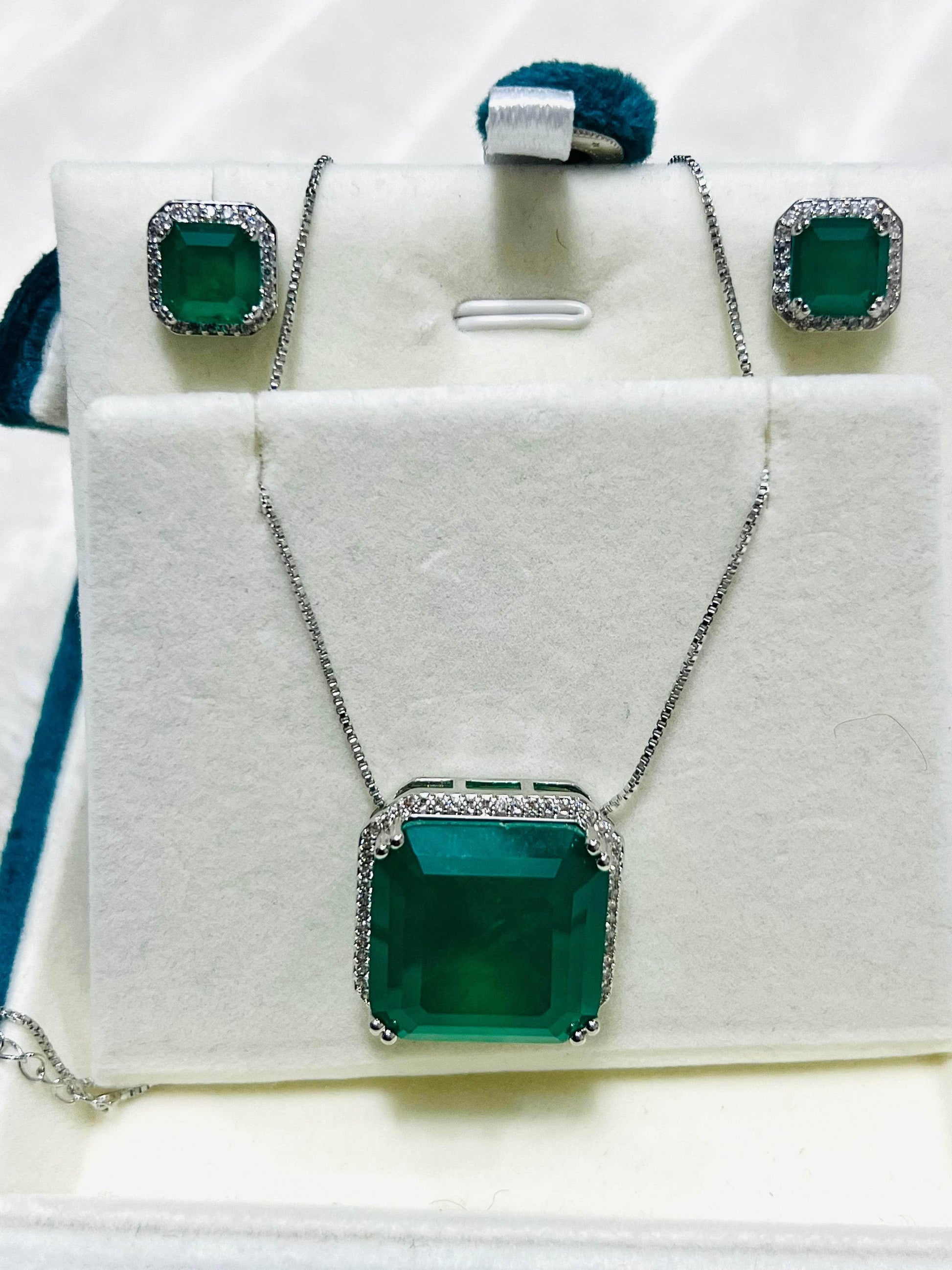 Emerald and diamond jewelry set including a necklace and earrings, neatly displayed in a white gift box.