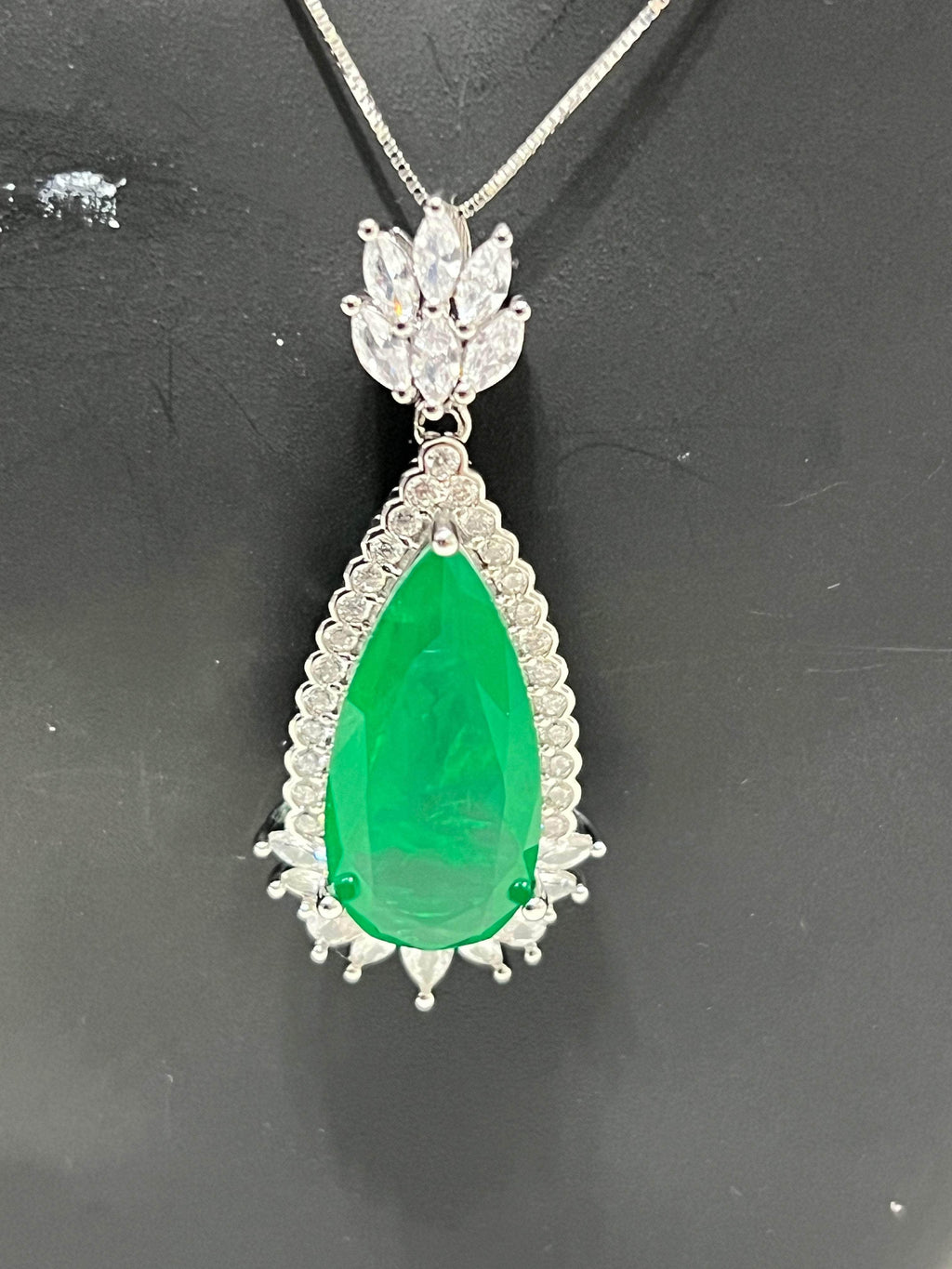 Close-up of a vibrant emerald doublet pendant featuring a large green teardrop stone surrounded by sparkling white accents.