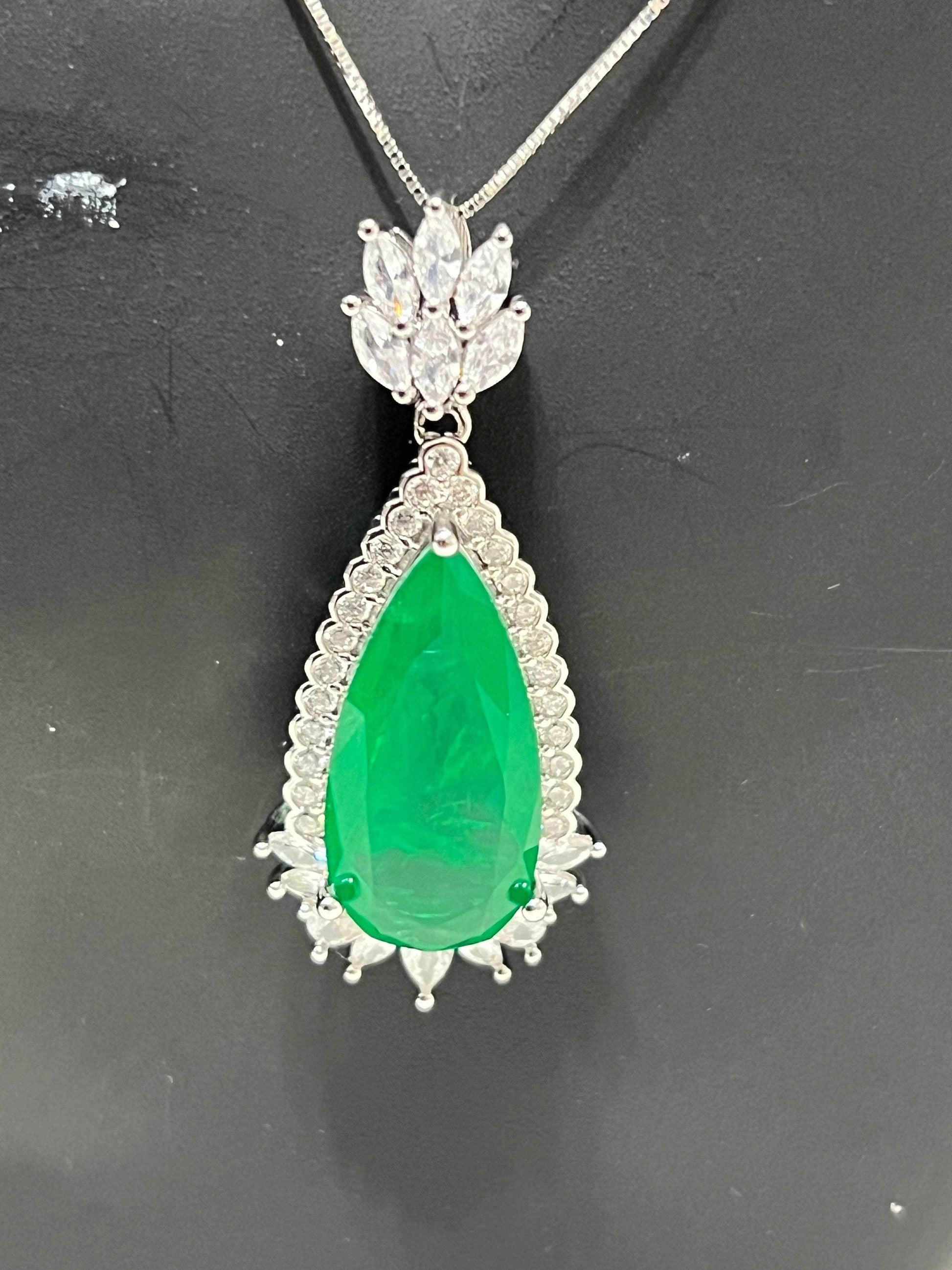 Close-up of a vibrant emerald doublet pendant featuring a large green teardrop stone surrounded by sparkling white accents.