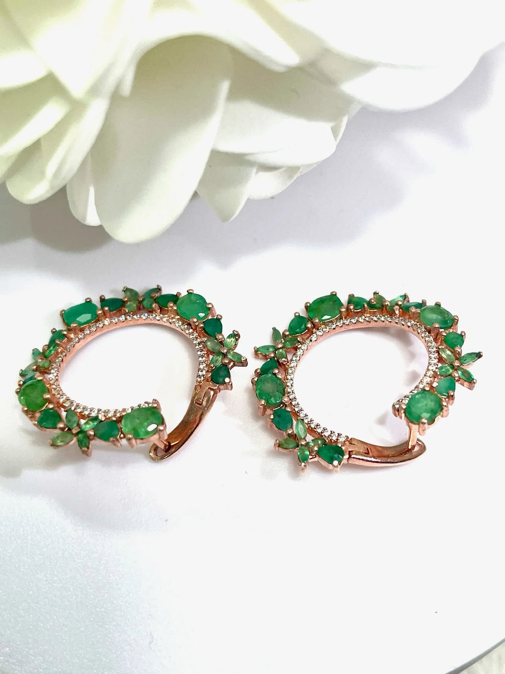 Close-up shot of two rose gold plated sterling silver hoop earrings with bright green Colombian emeralds and diamond accents
