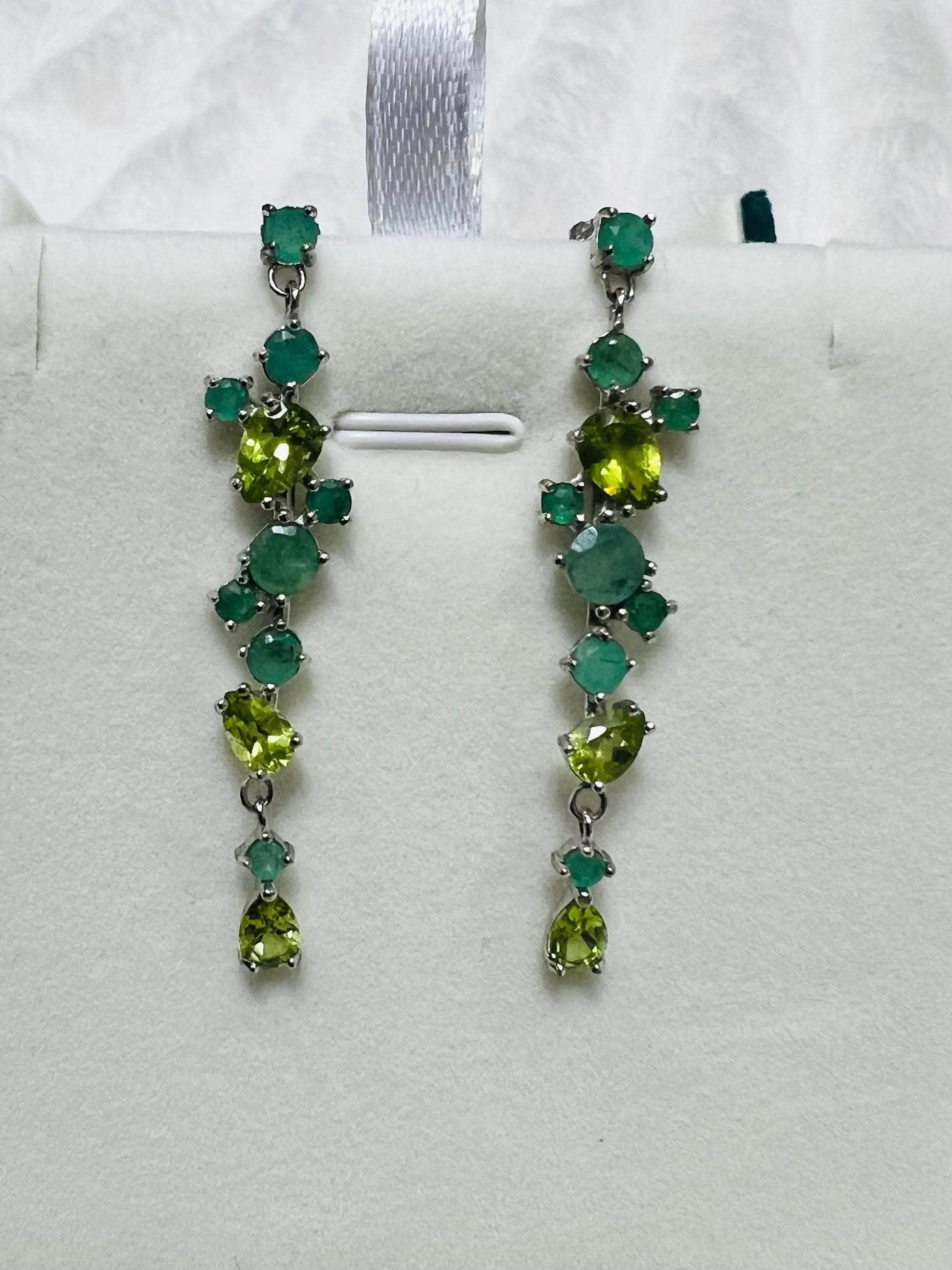 Close-up of vibrant emerald and peridot long drop earrings in sterling silver, showcasing natural green gemstones.