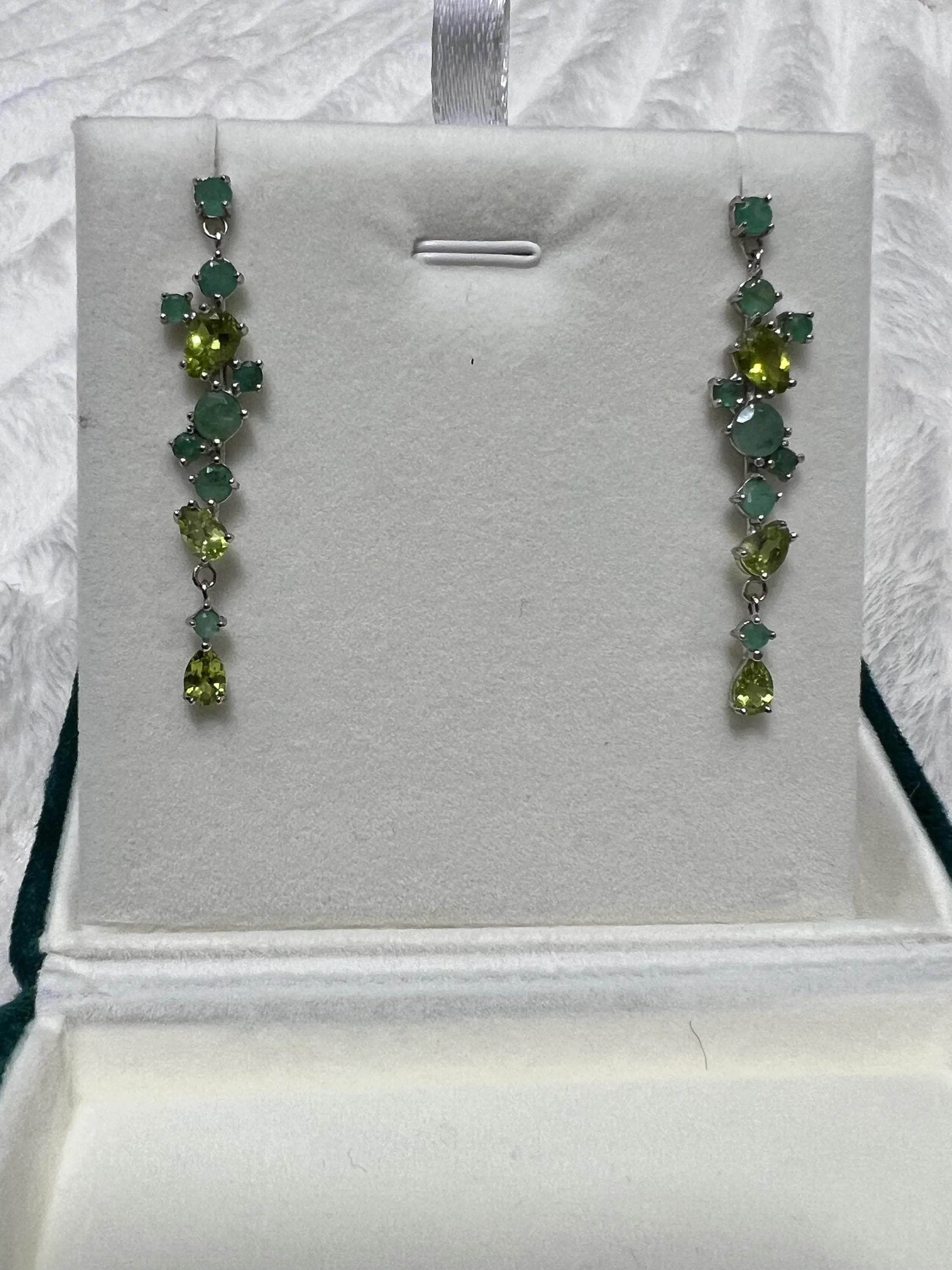Full view of elegant emerald and peridot long drop earrings on a white jewelry display. Perfect for women.