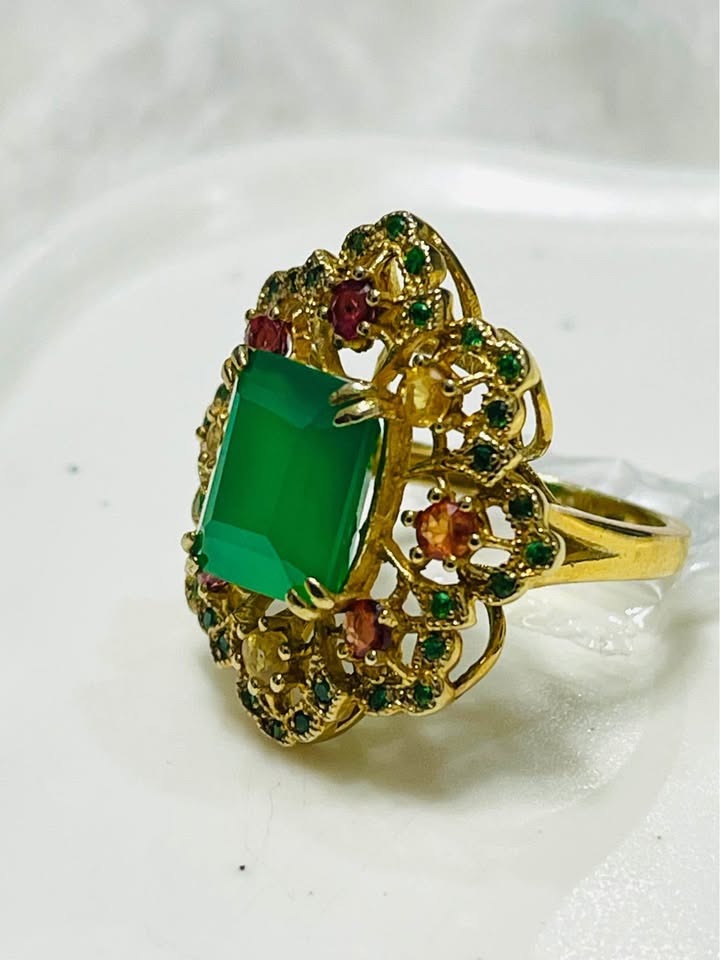 A luxurious cocktail ring featuring a large green agate with surrounding emeralds, sapphires, and diopside stones.