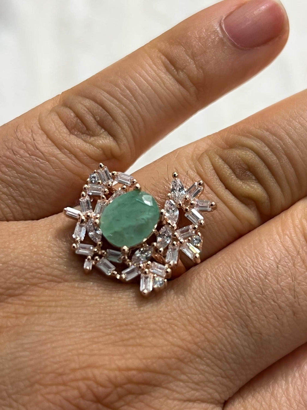Elegant vintage emerald and sapphire cluster ring worn on a finger, showcasing its unique design and sparkle.
