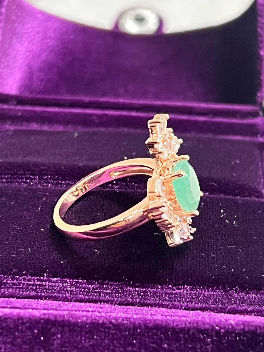 Side profile of a vintage emerald and sapphire ring, highlighting the rose gold band and setting in a jewelry box.
