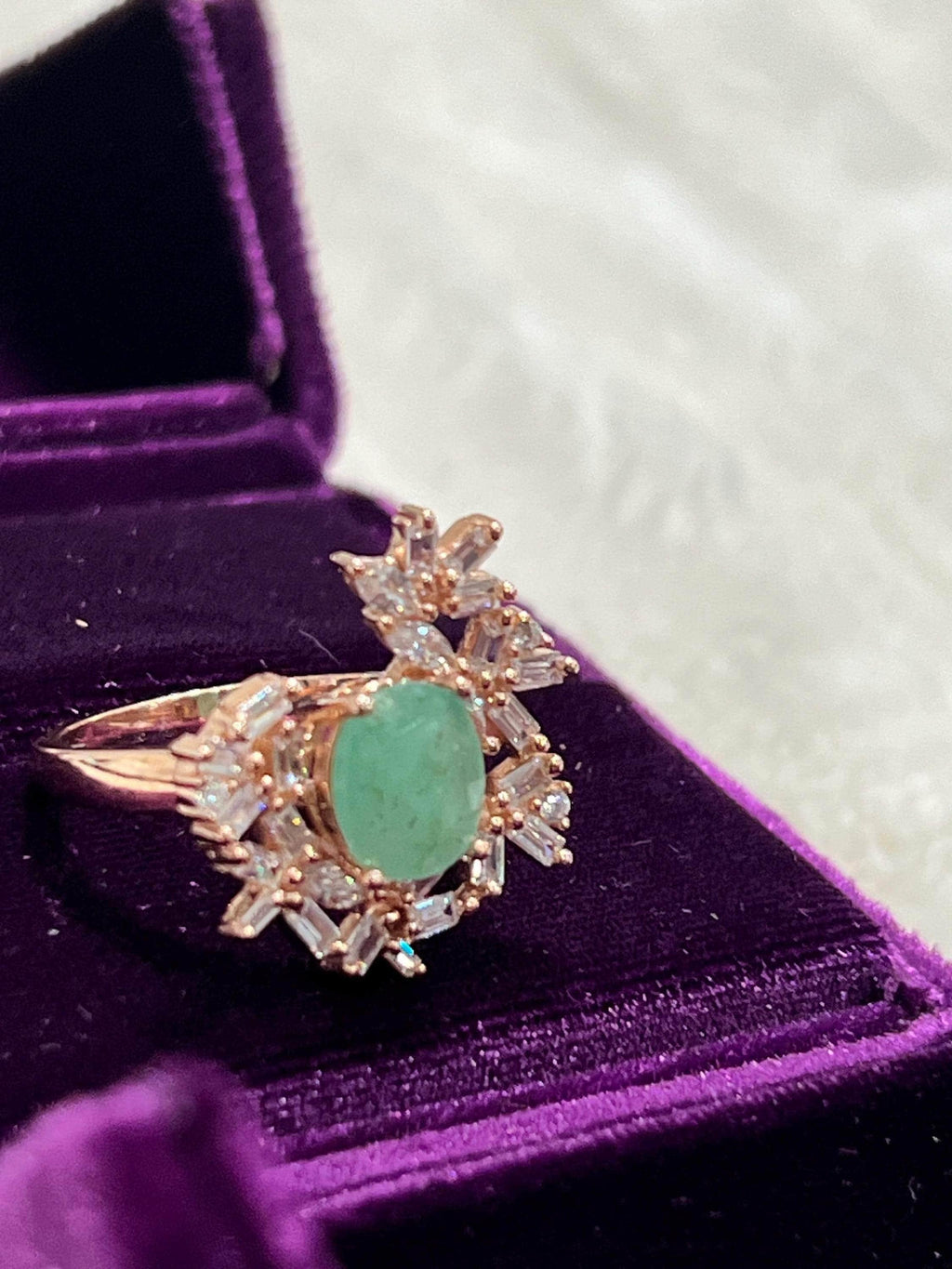 Top-down view of a dazzling vintage emerald and sapphire ring, set in rose gold, displayed in a purple box.