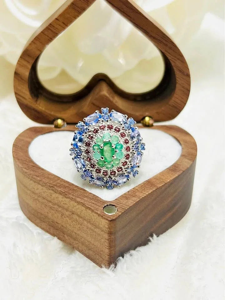 An exquisite cluster ring featuring a central emerald, surrounded by rhodolite and tanzanite gems.
