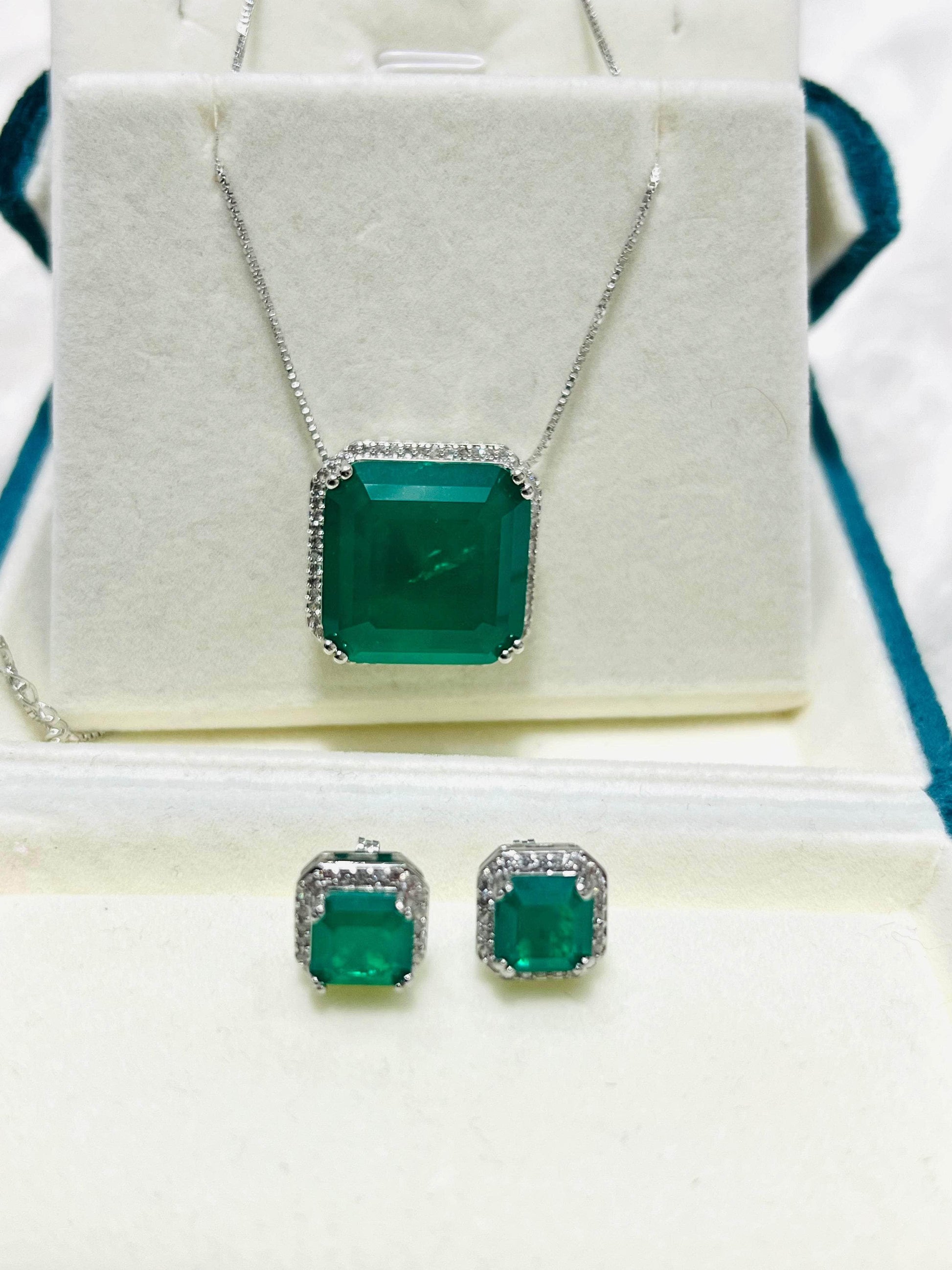 Complete emerald and diamond jewelry set, including a pendant necklace and two earrings, presented on a white display.