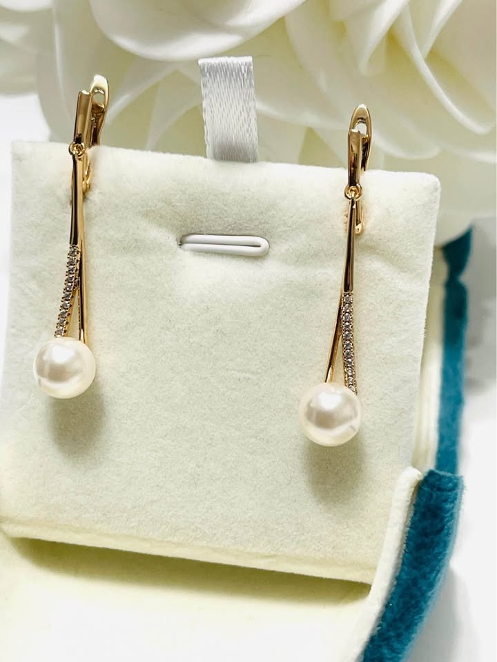 Angled view of a pair of gold-filled long dangle earrings, each adorned with a lustrous pearl.