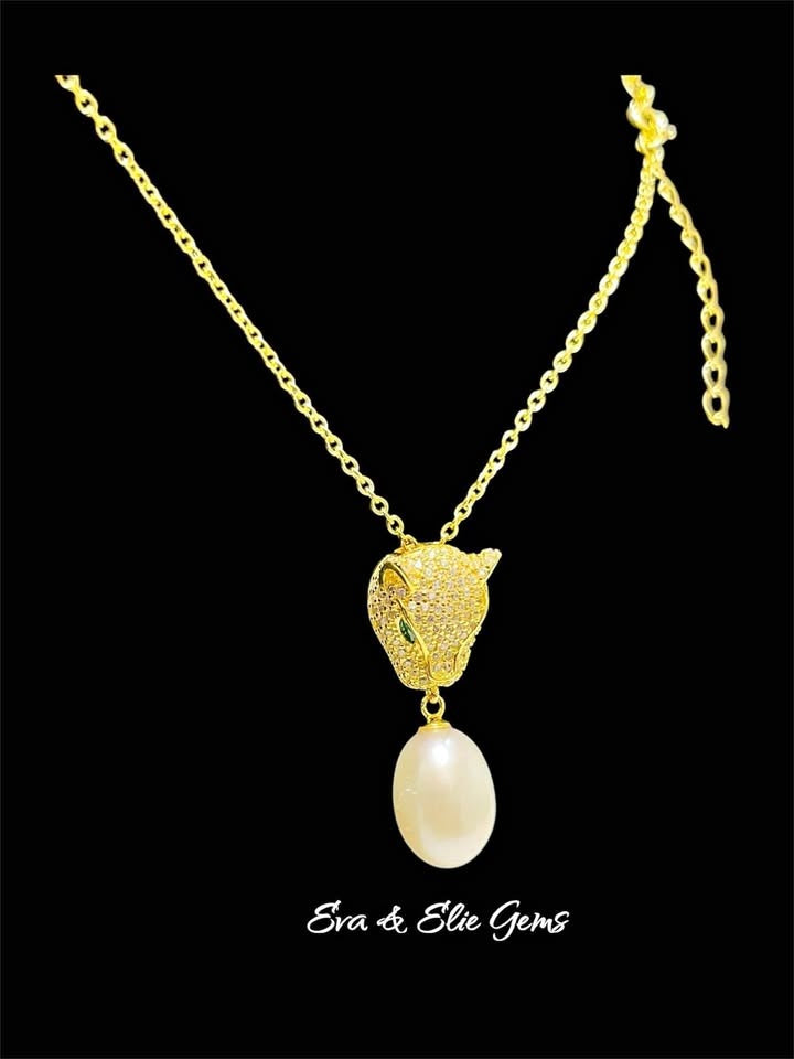 Luxurious gold panther necklace with emerald eyes and a South Sea pearl on a dark background.