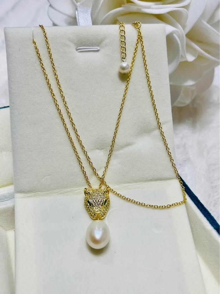 Elegant gold panther necklace featuring emerald eyes and a South Sea pearl in an open jewelry box.