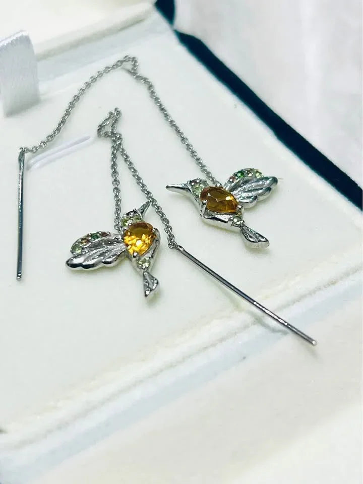 Angled view of a pair of hummingbird ear threader earrings with natural citrine and peridot gemstones.