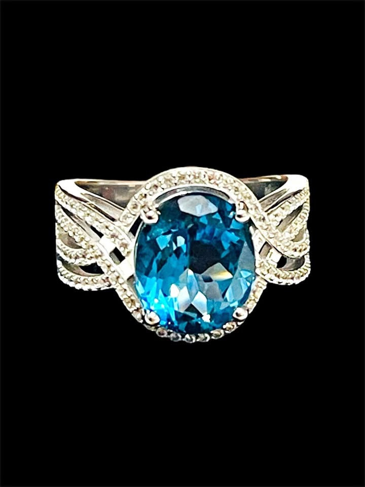 Elegant London blue topaz and diamond ring, featuring a vibrant oval topaz, displayed on white.