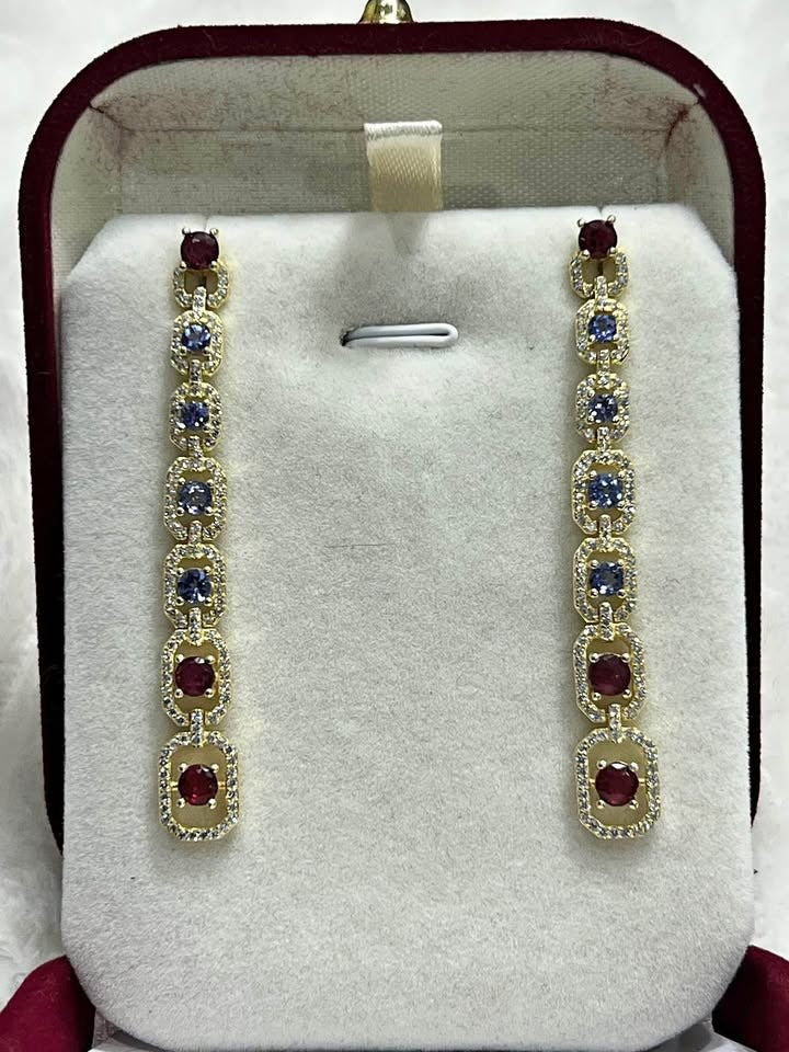 Long gemstone earrings with deep red rubies and vibrant blue tanzanite, set in sterling silver.