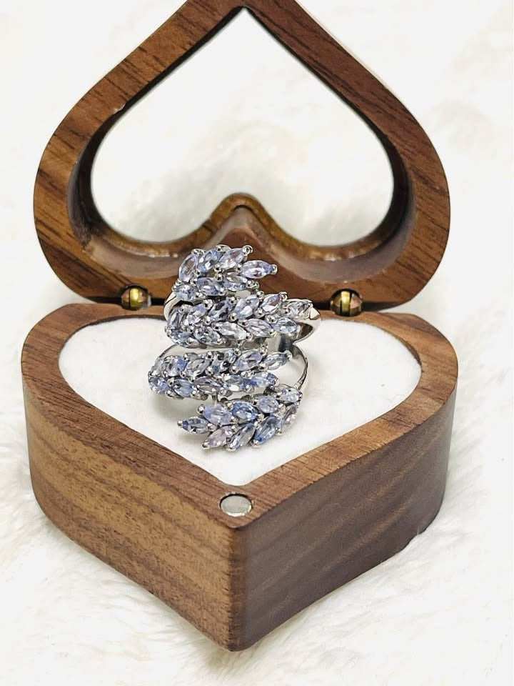 Front view of a sterling silver ring with marquise tanzanite clusters, resting in a wooden heart box.