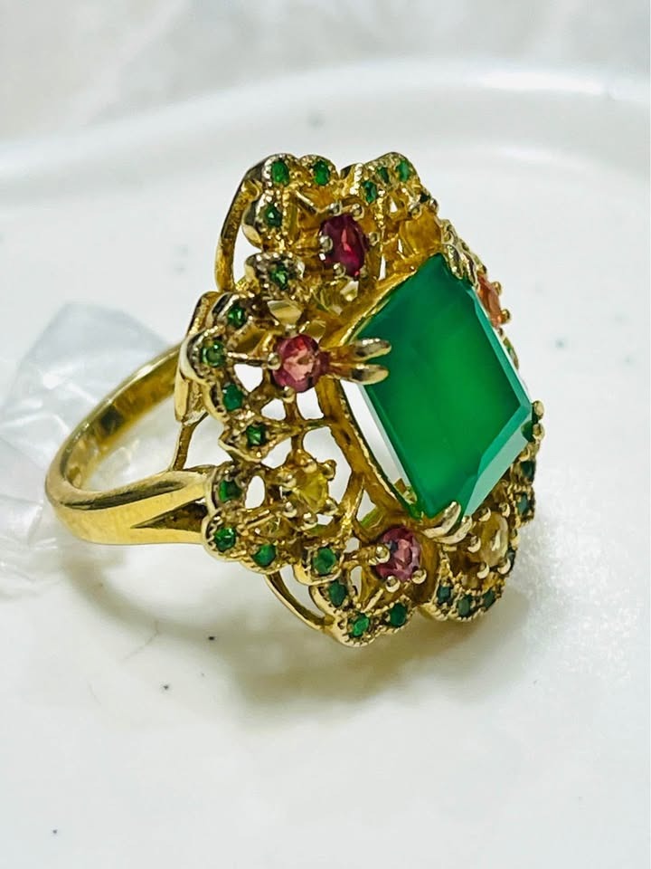 Ornate floral design ring with a natural green agate centerpiece and a halo of emeralds, sapphires, and diopside.
