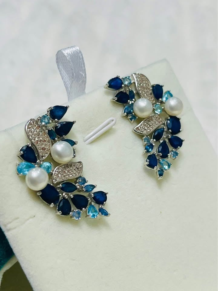 Elegant cluster earrings with dark blue sapphires, light blue topaz, and white pearls on a silver setting.