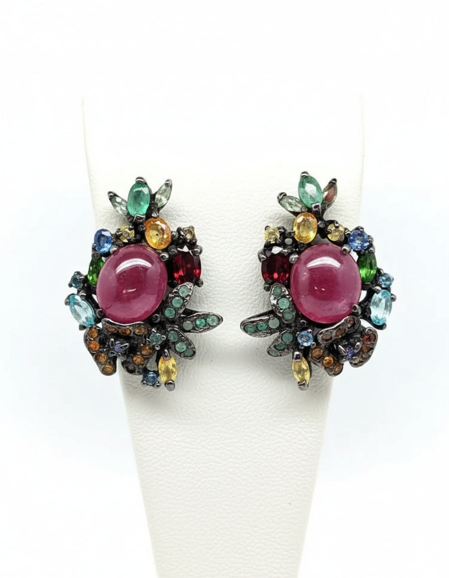 A pair of intricate cluster earrings with natural ruby, emerald, and sapphire gemstones in a unique dark metal setting.